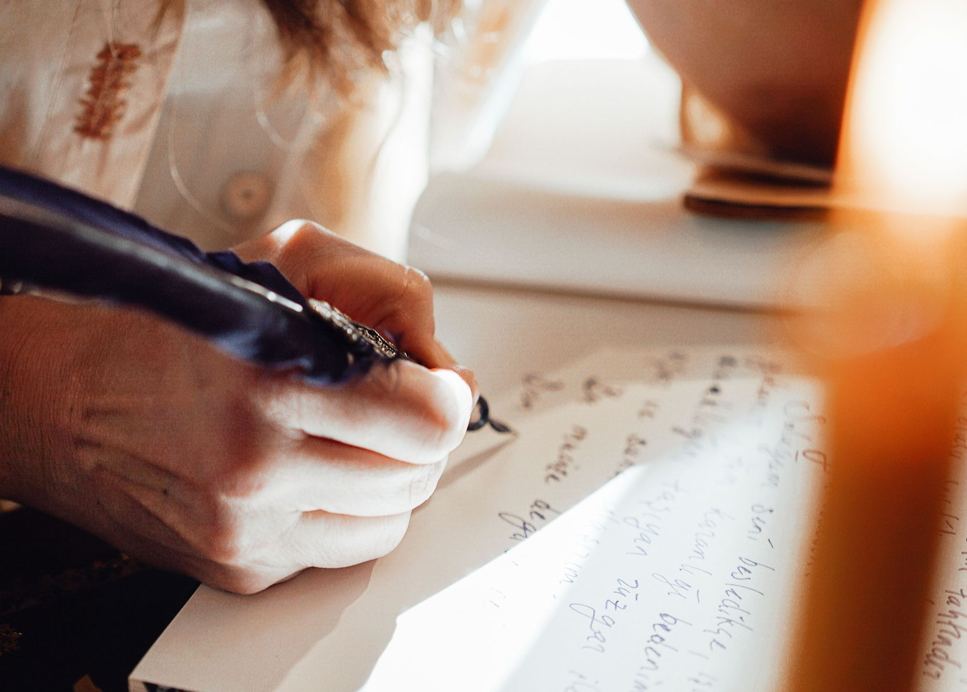 Close-up of a hand writing in a notebook with a dark pen in warm light
