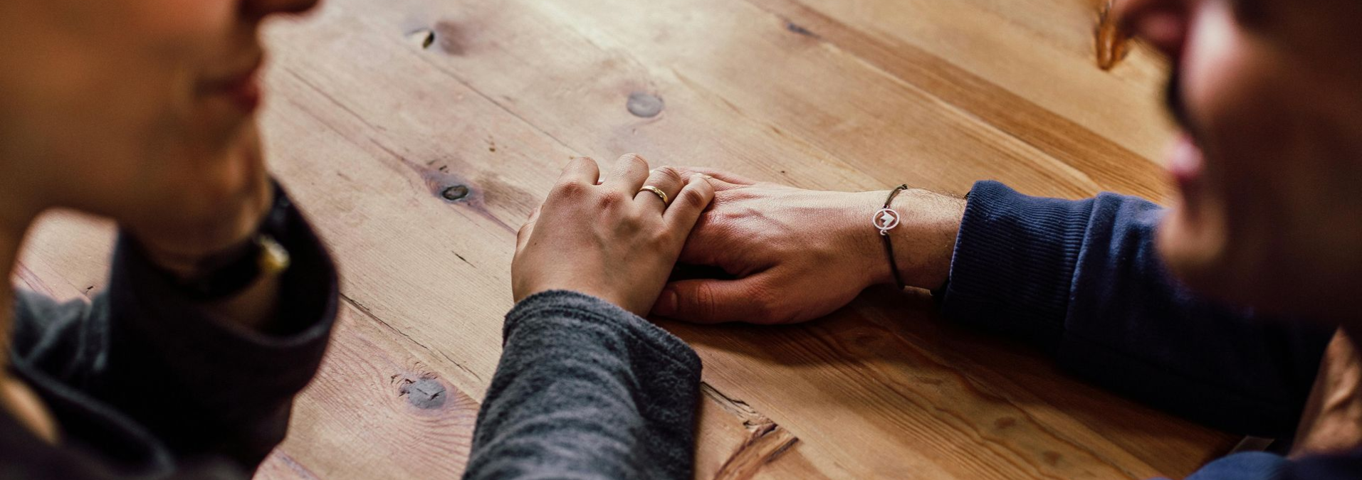 Hands clasped across a wooden table in a warm, close-up scene