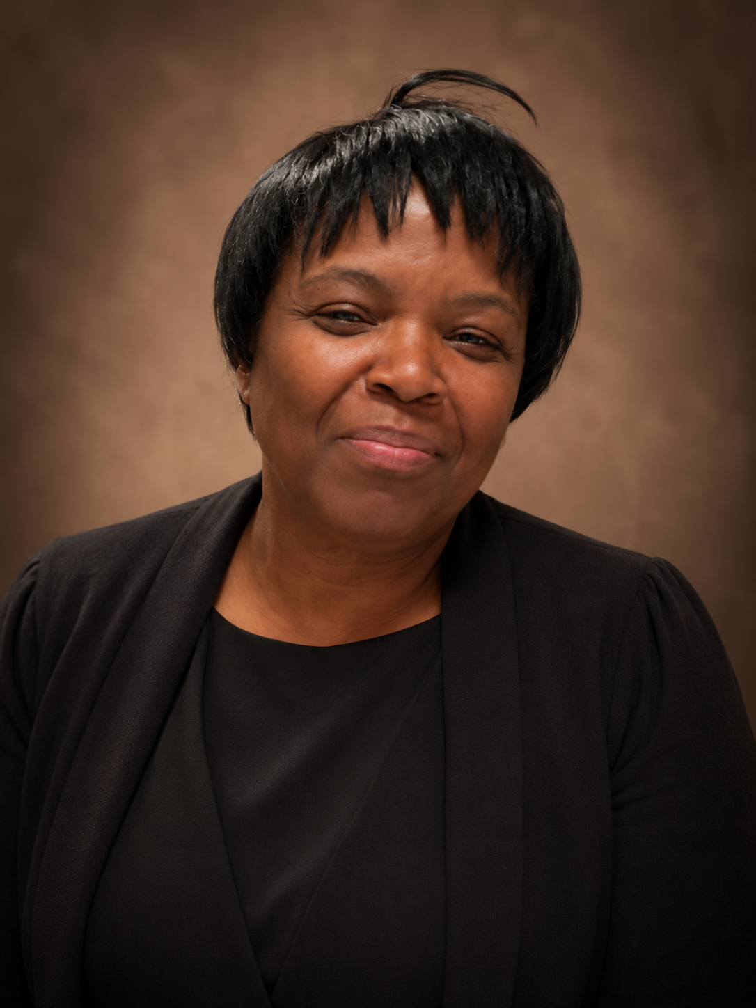 Smiling woman in black top and jacket against a warm brown studio backdrop