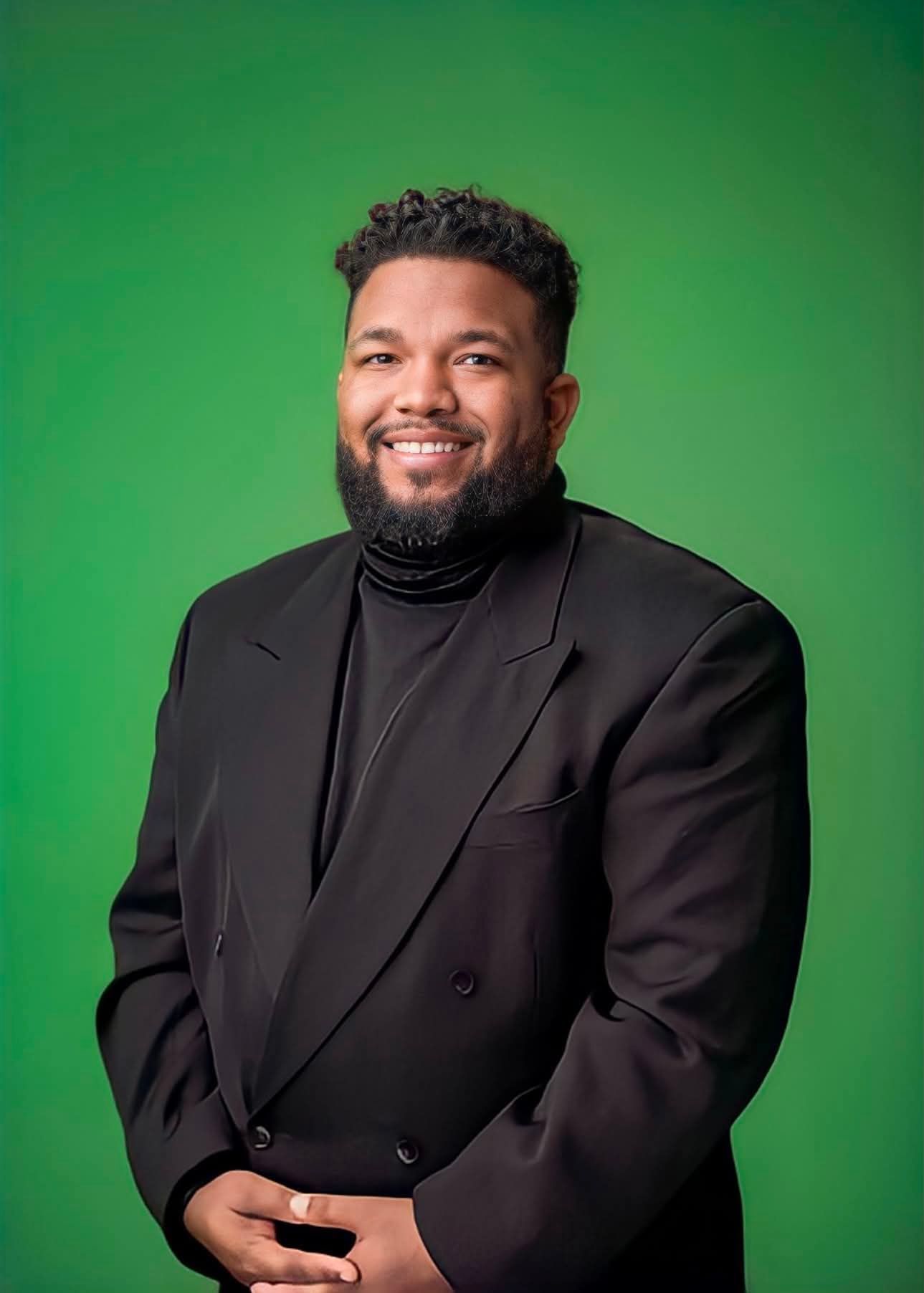 Smiling person in a black suit against a green background