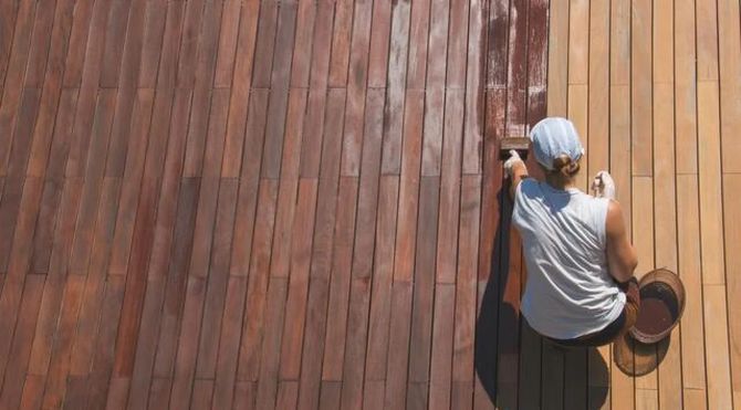 Person painting a wooden deck with a roller, viewed from above.