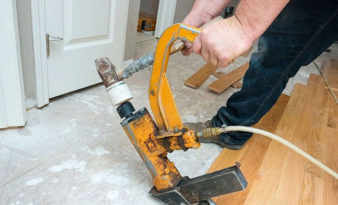 Person using a yellow floor scraper to remove adhesive from a wooden floor indoors.