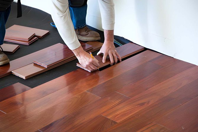 Workers applying a glossy floor coating with a bucket and roller in a room under renovation