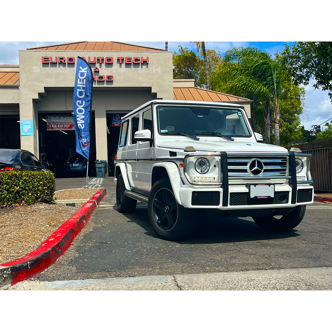 White Mercedes SUV parked outside a car dealership with a red curb and blue banner