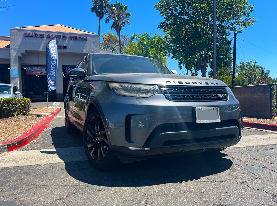 Dark gray SUV parked outside a dealership with a red curb and trees in the background | Euro Auto Tech & Smog