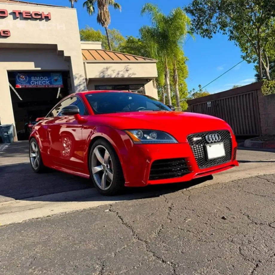 A red Audi sedan parked outside of an automotive repair shop with a Smog Check sign in the background | Euro Auto Tech & Smog