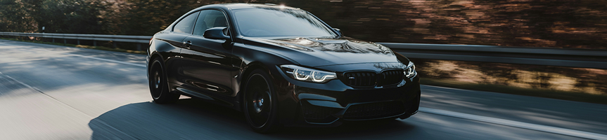 Black sedan driving on a road, motion blur in the background.