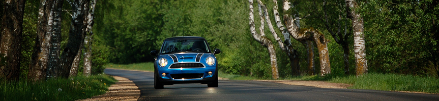 Blue car driving on a tree-lined road with green foliage overhead