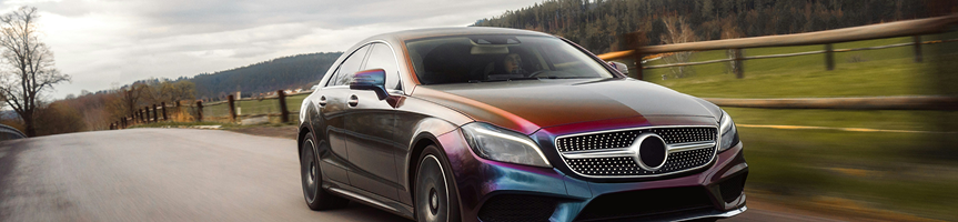 Black Mercedes sedan driving on a road in a rural landscape at sunset