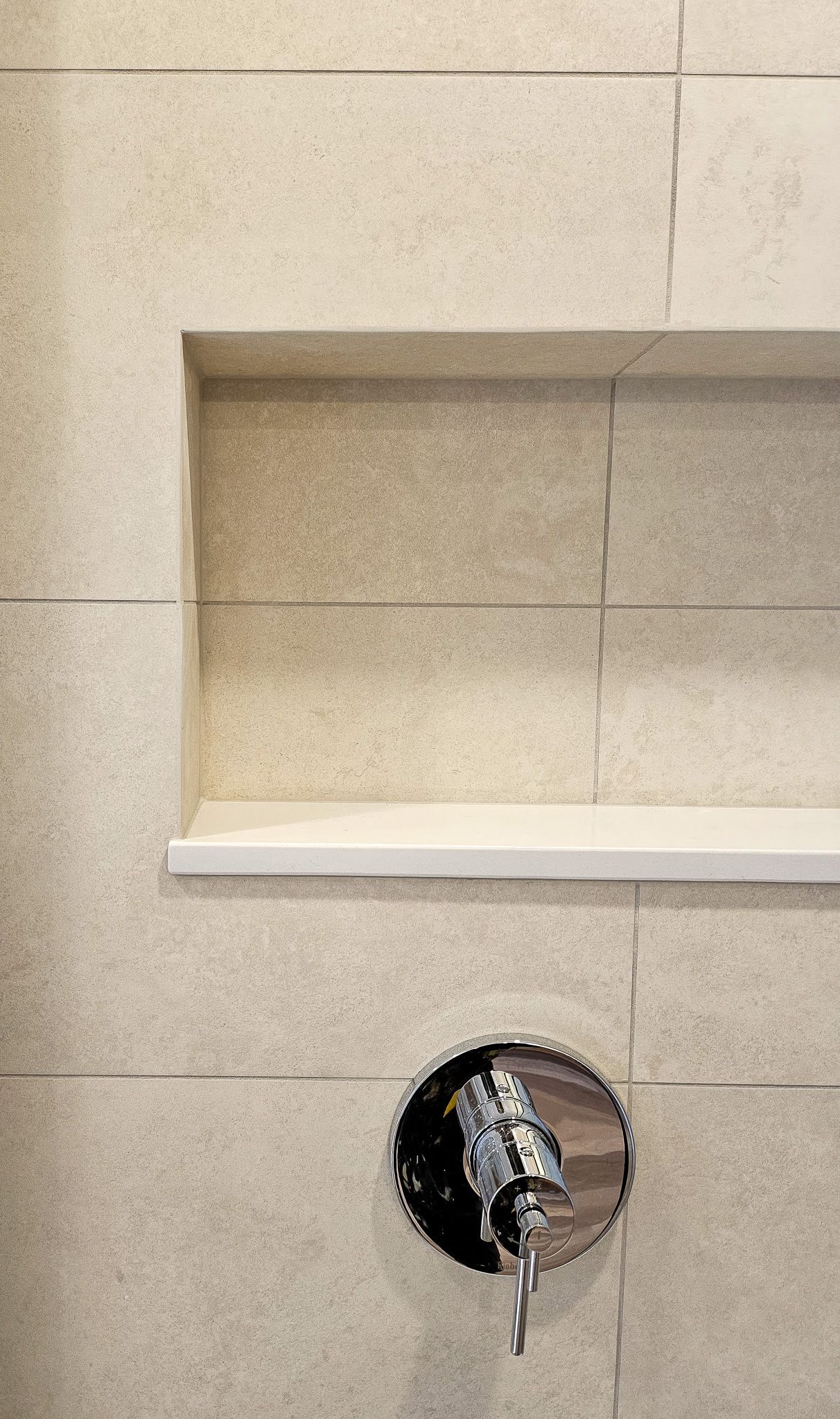 A close up of a bathroom wall with a shelf and a shower head.