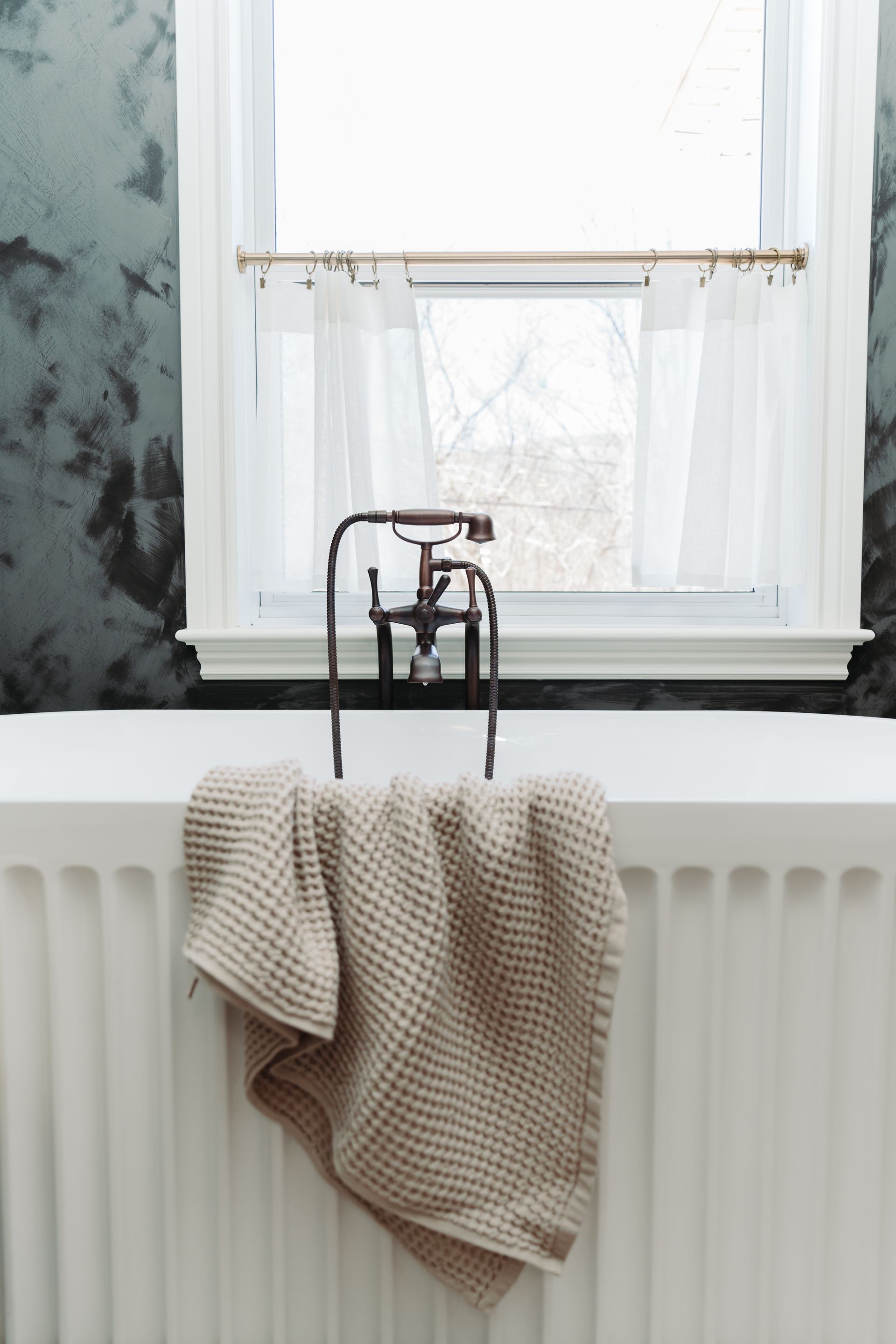 A bathtub with a towel hanging over it in a bathroom next to a window.