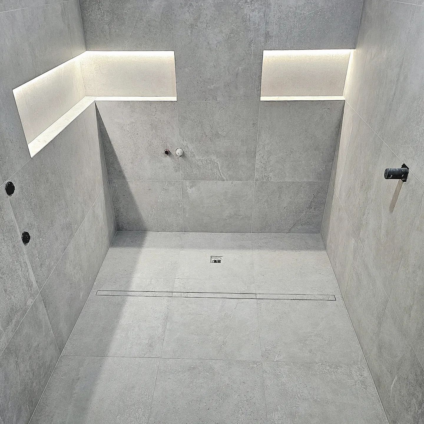 A bathroom with a walk in shower and a drain.