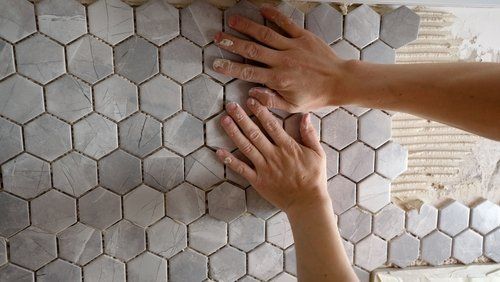 A person is laying tiles on a wall with their hands.
