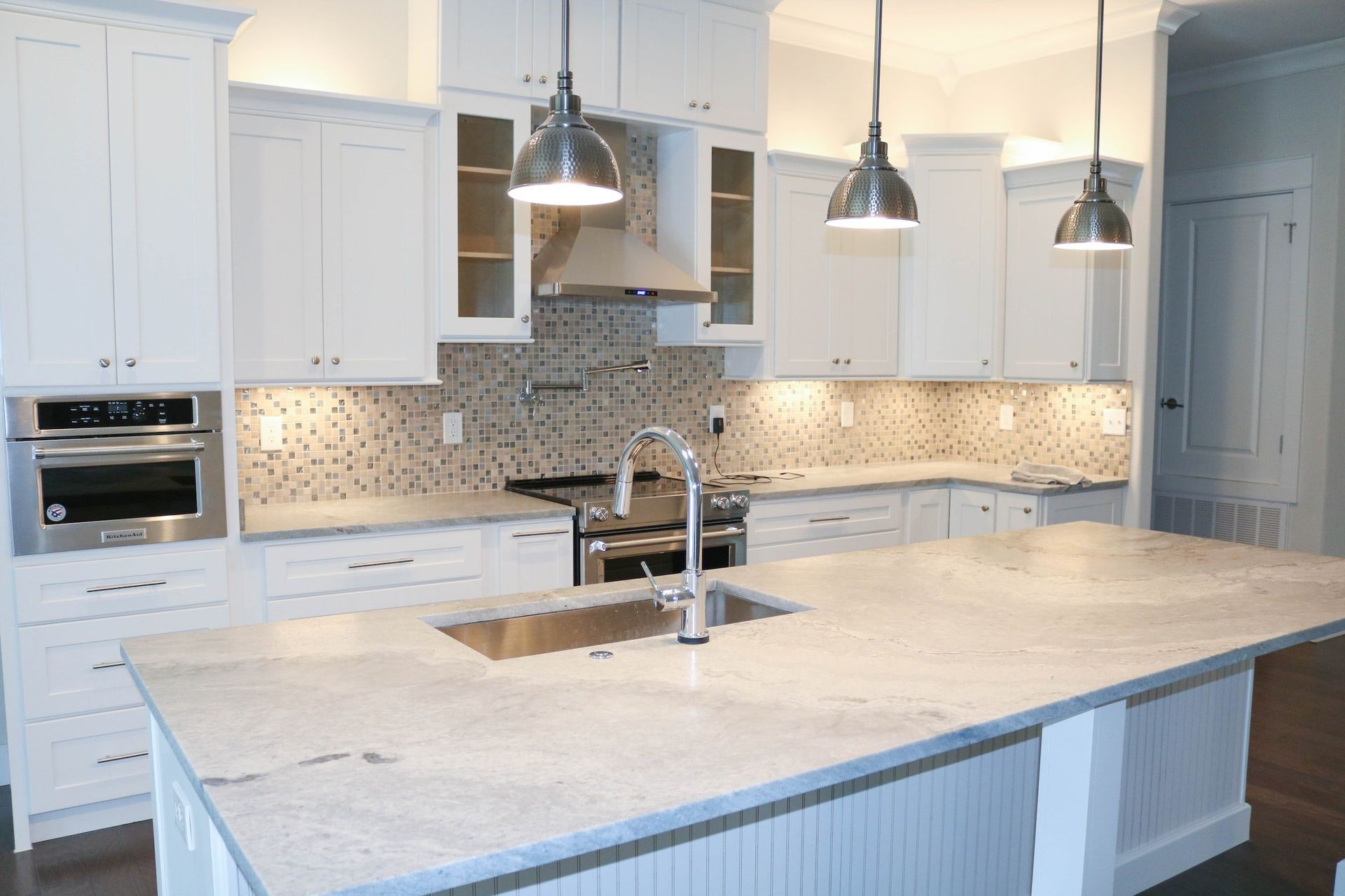 A kitchen with white cabinets , stainless steel appliances , a large island and a sink.