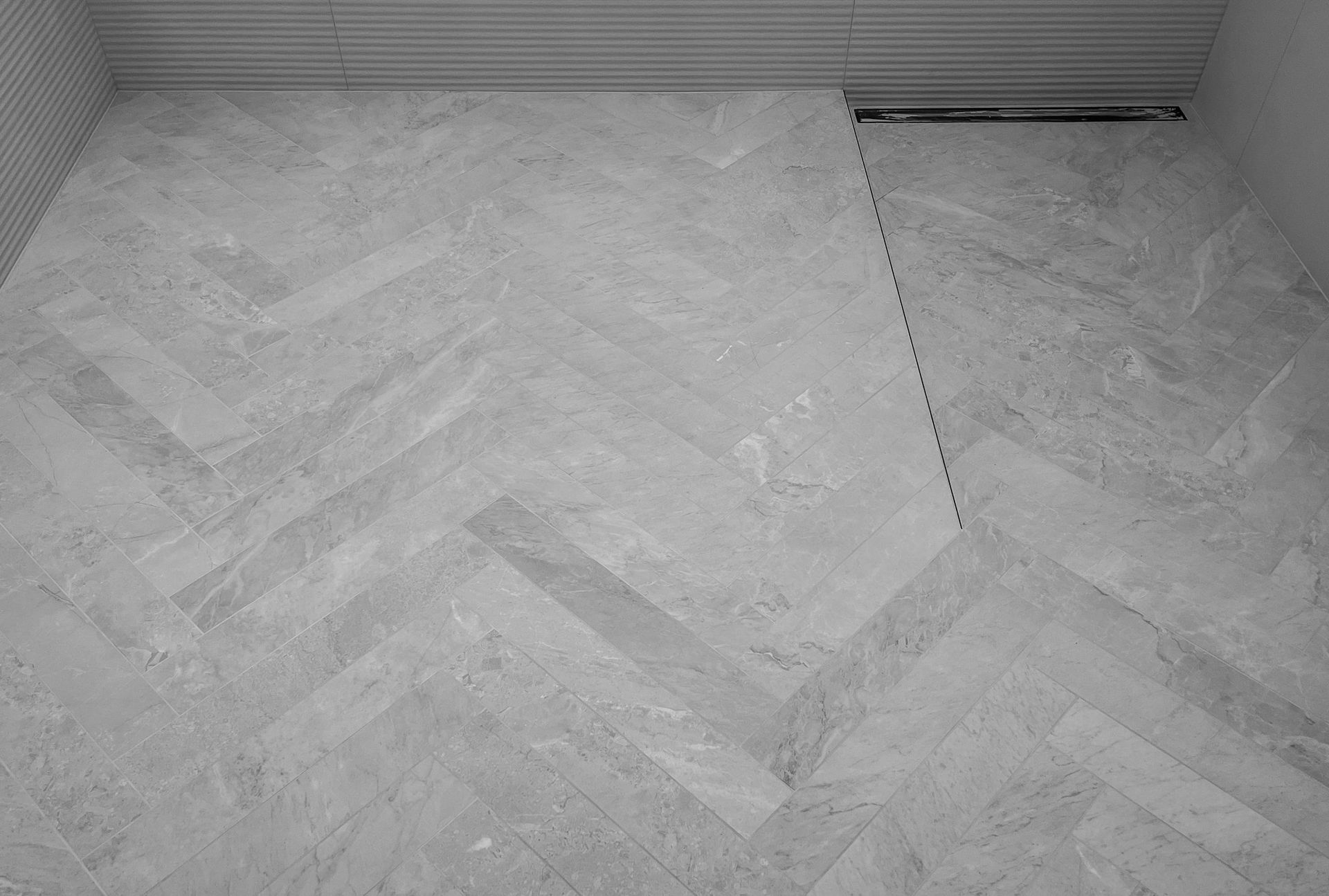 A bathroom floor with a herringbone pattern and a drain.