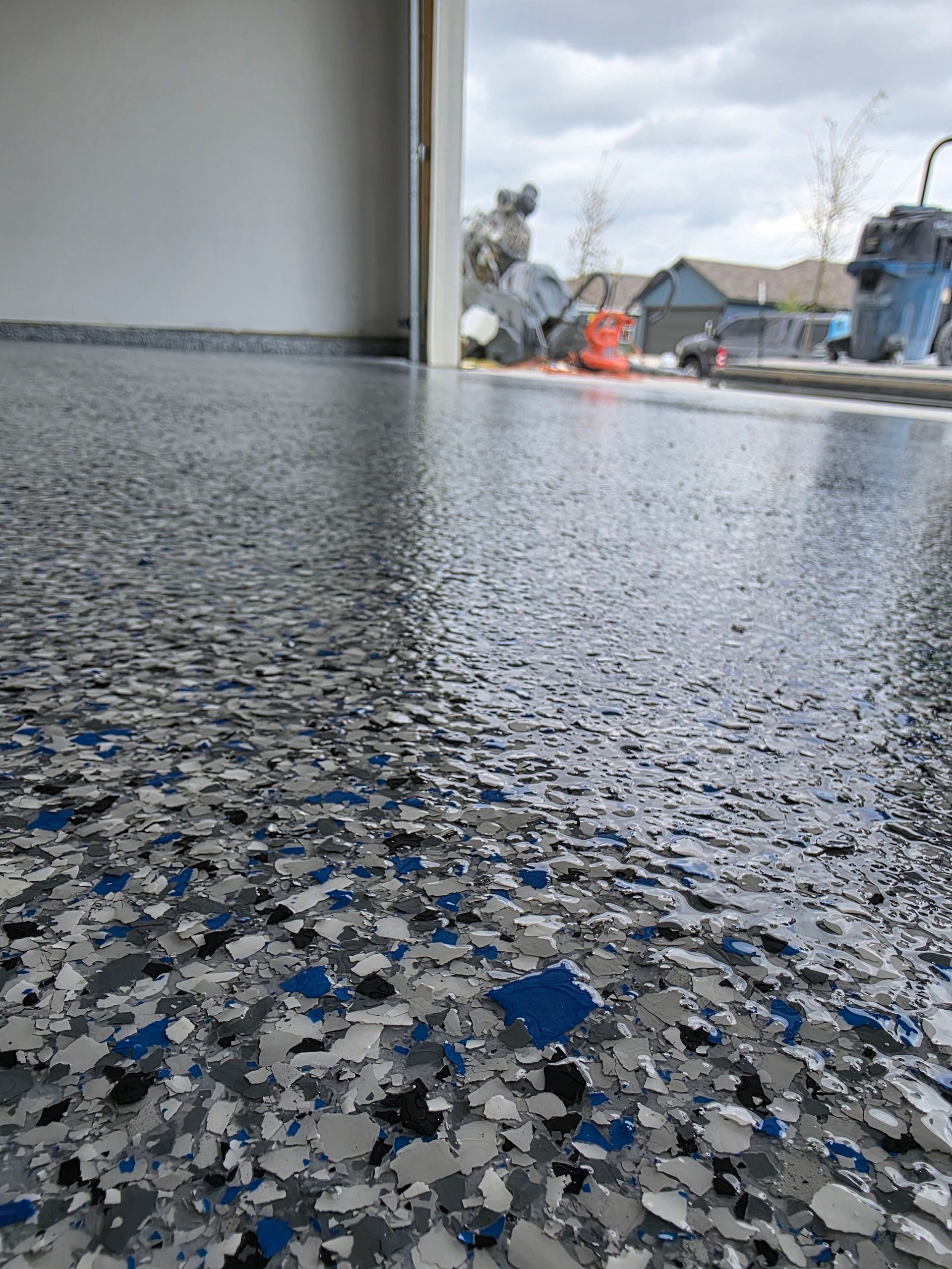 Close-up of a wet, speckled floor under a covered outdoor area, with houses in the distance.