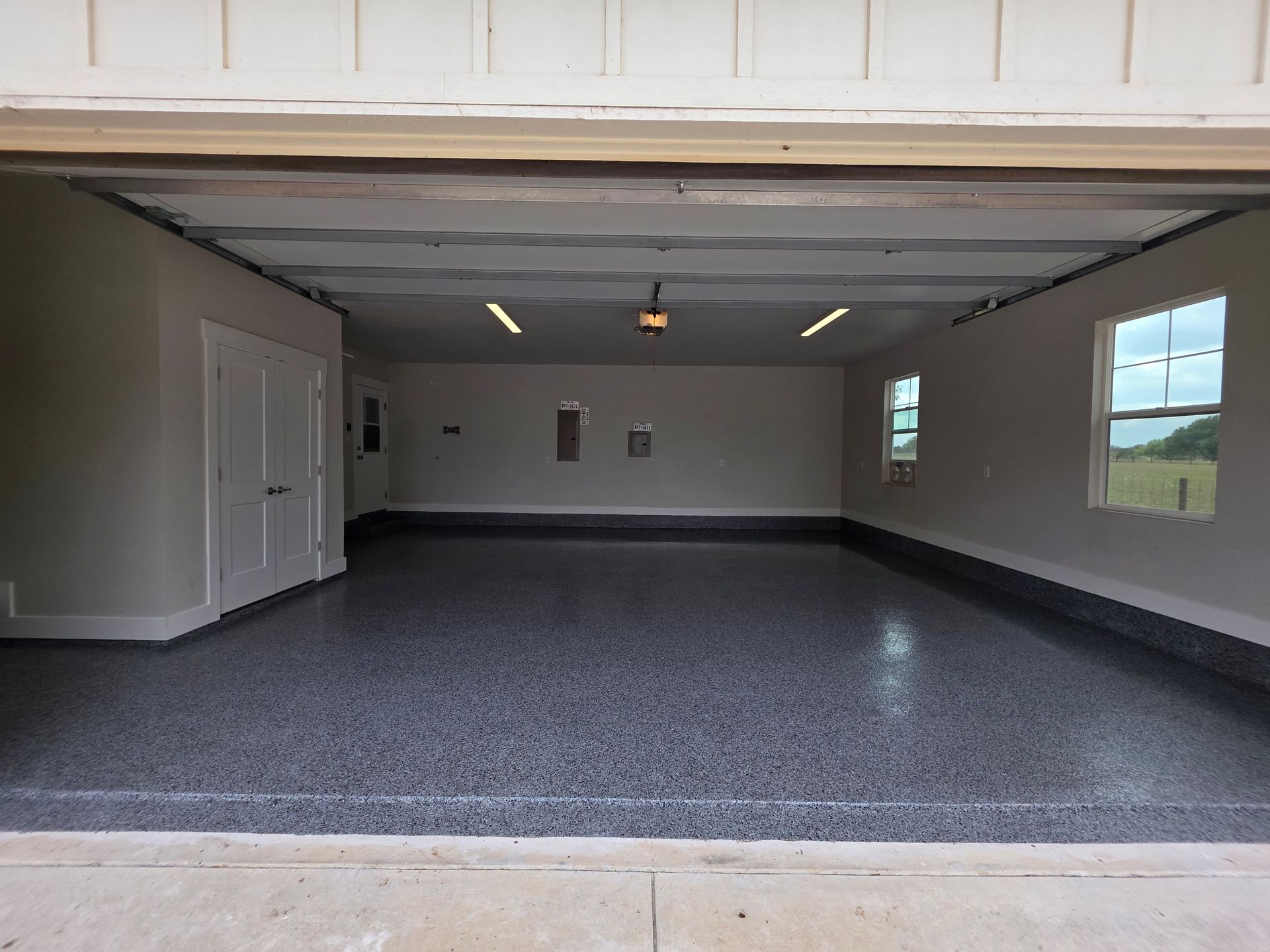 Empty open garage with gray speckled floor, white walls, and windows on the right.