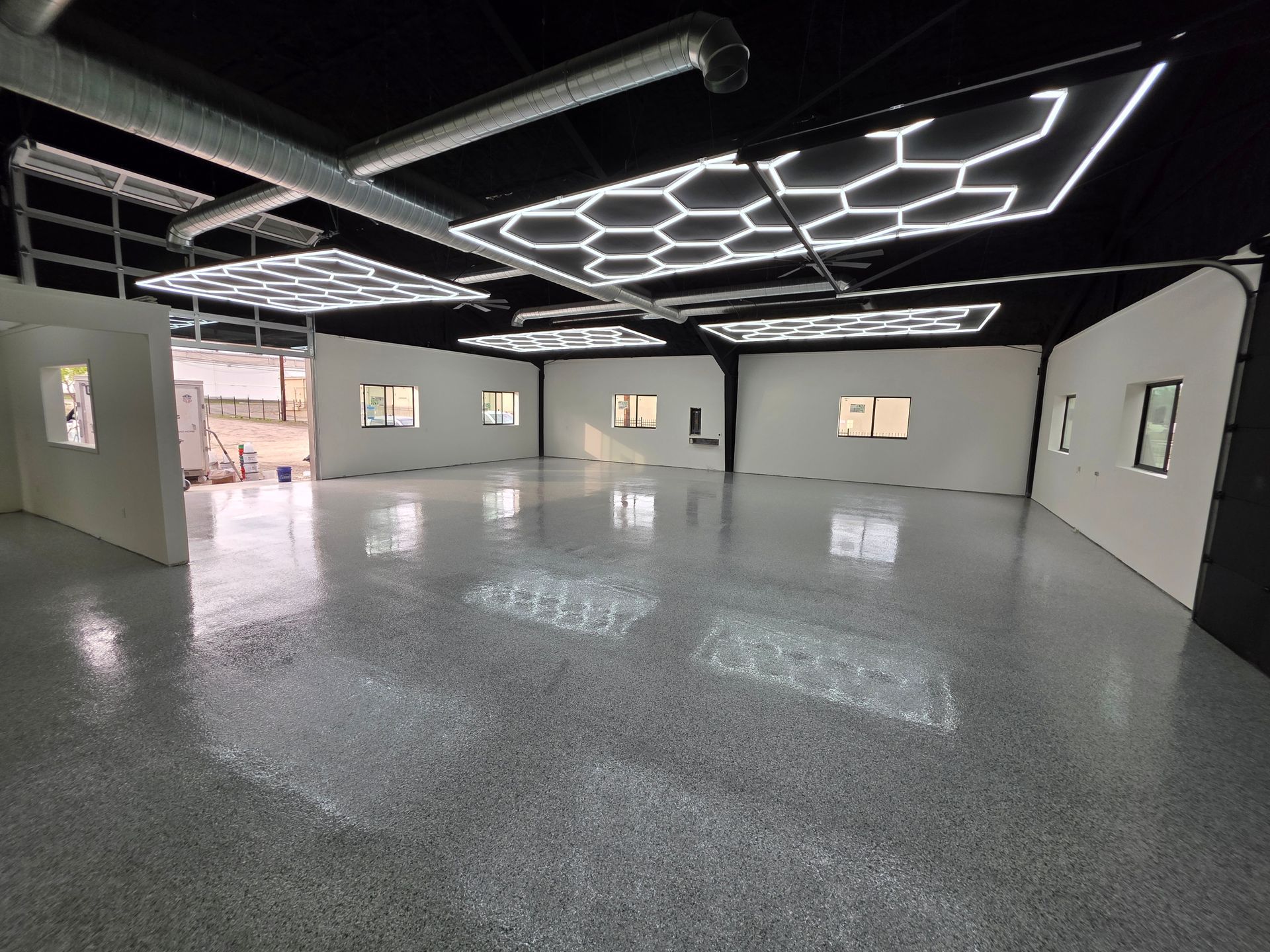 Empty modern office space with glossy gray floor, white walls, and geometric ceiling lights
