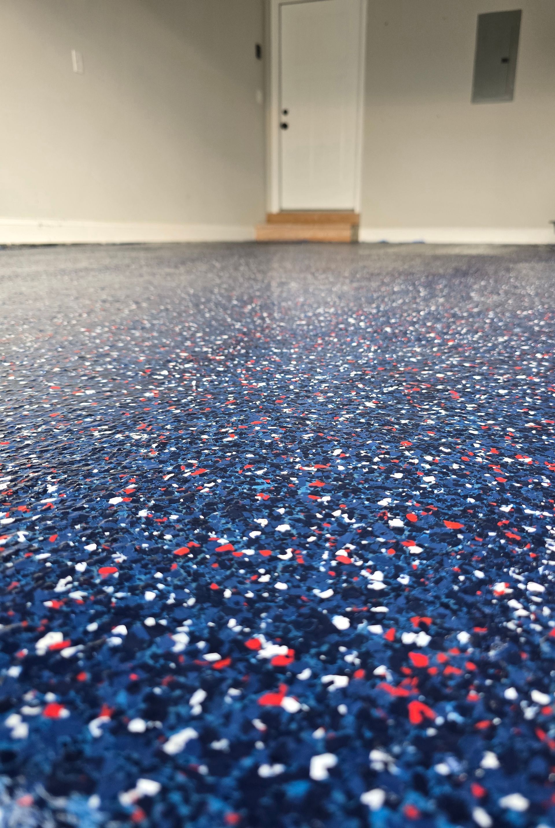 Low-angle view of blue speckled carpet in an empty room with a closed white door and gray wall panel.