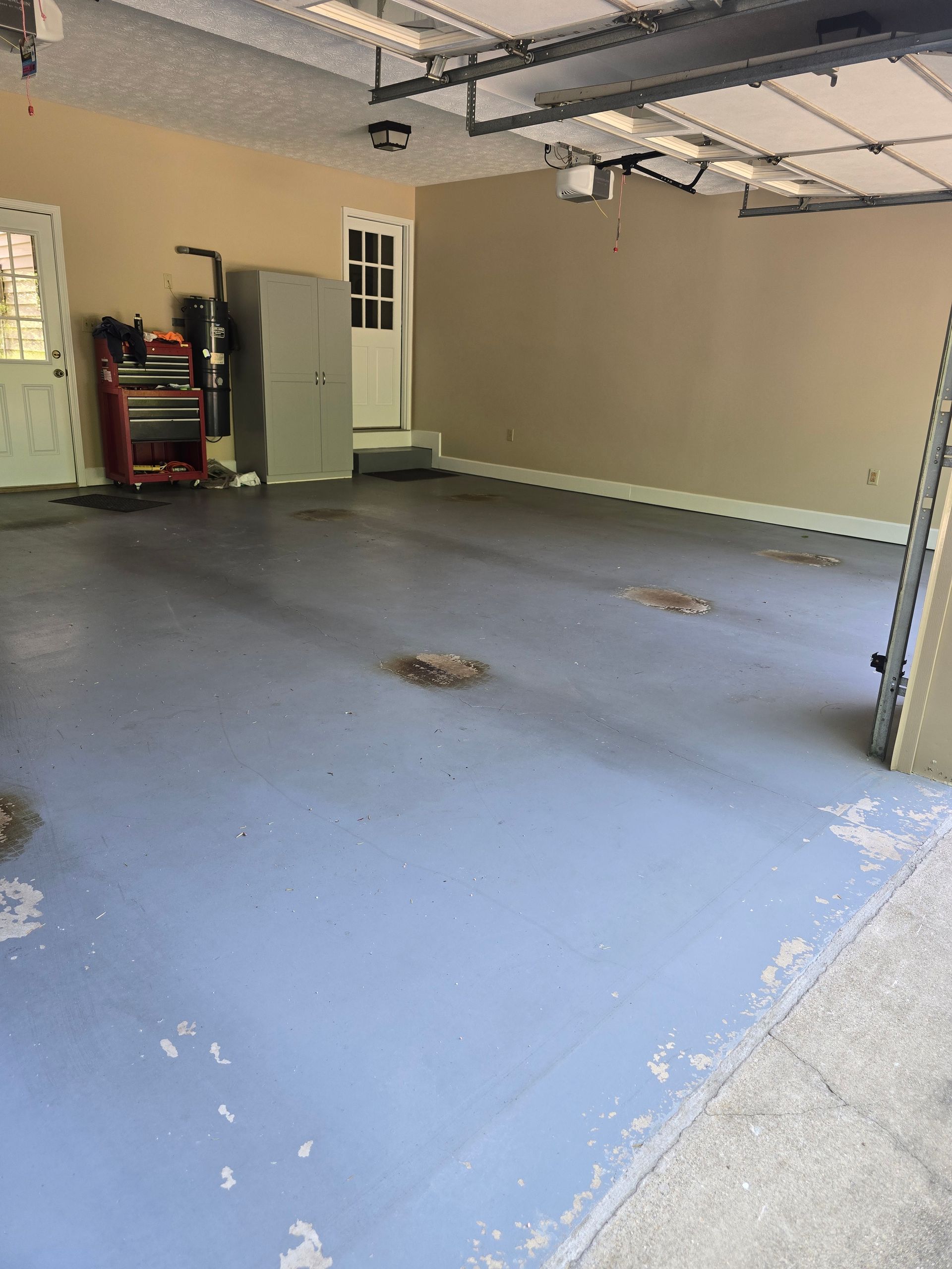Empty garage with gray floor, beige walls, and an open garage door near a shelving unit.