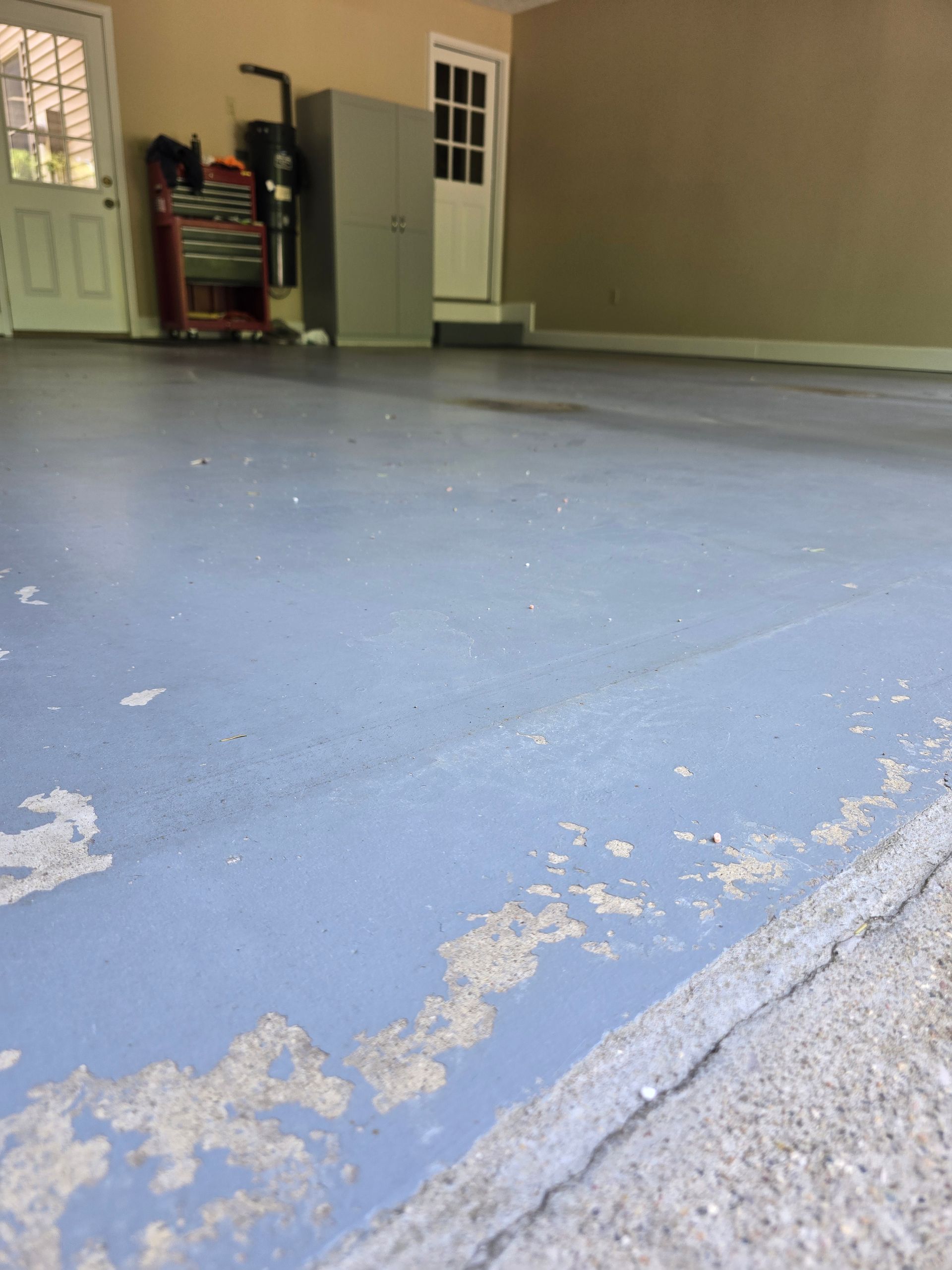 Blue painted concrete floor in an empty garage or workshop with peeling edges.