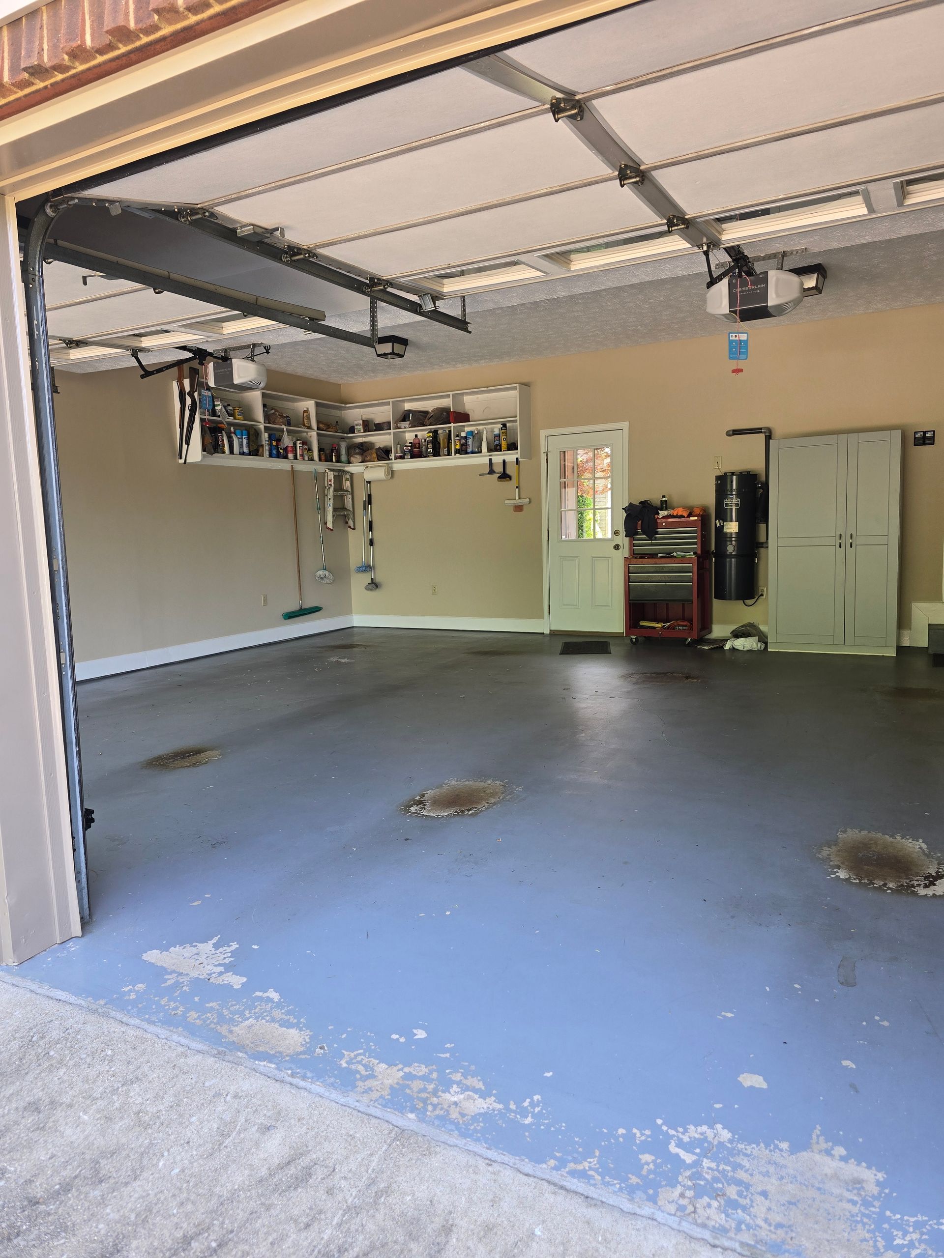 Empty garage with open door, blue concrete floor, and storage cabinets along the back wall