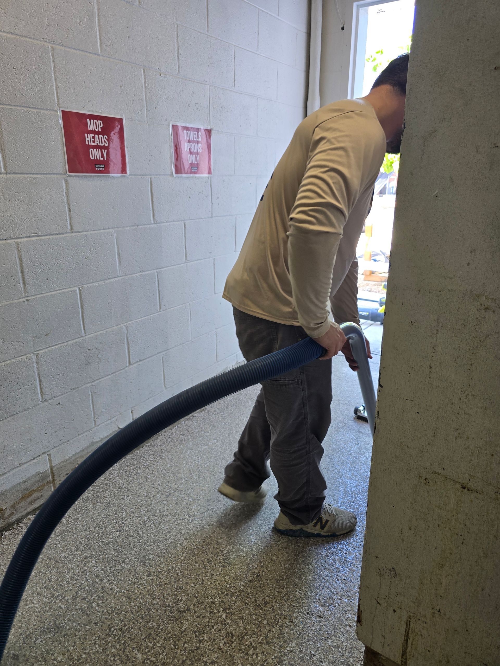 Worker vacuuming a speckled floor near a doorway in a white brick room