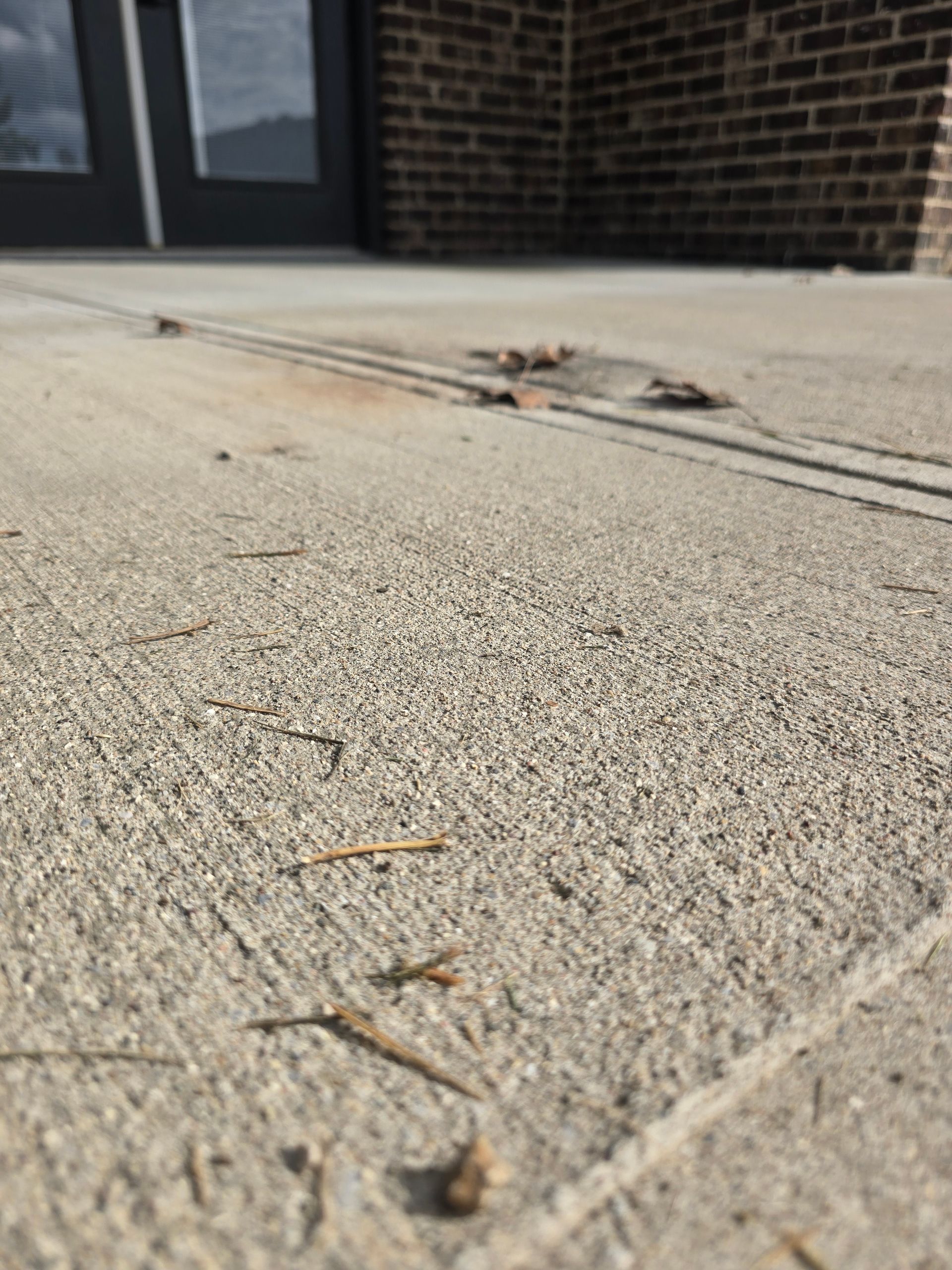 Close-up of cracked concrete sidewalk with debris near a brick building entrance