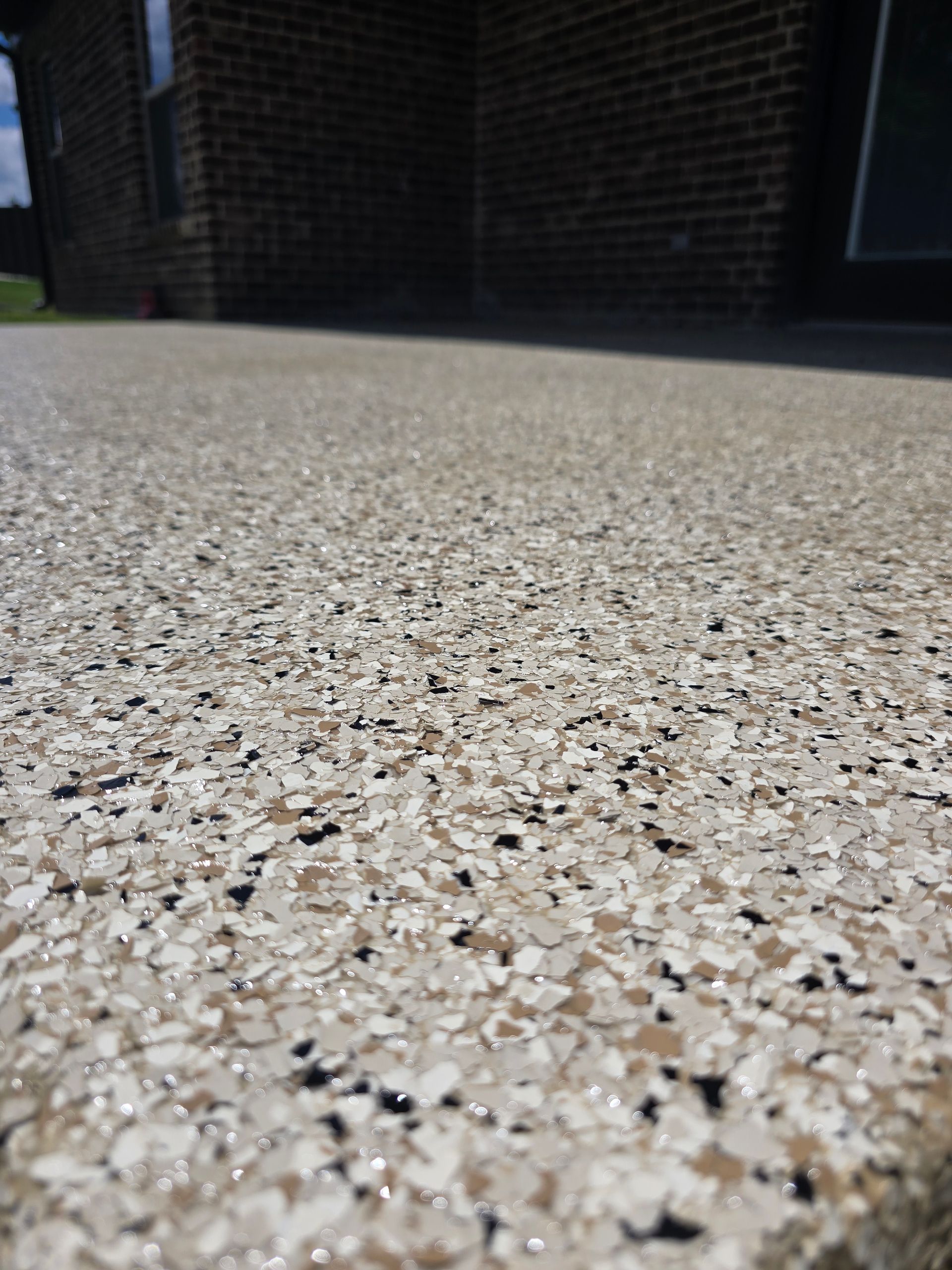 Close-up of speckled concrete pavement beside a dark brick building wall.