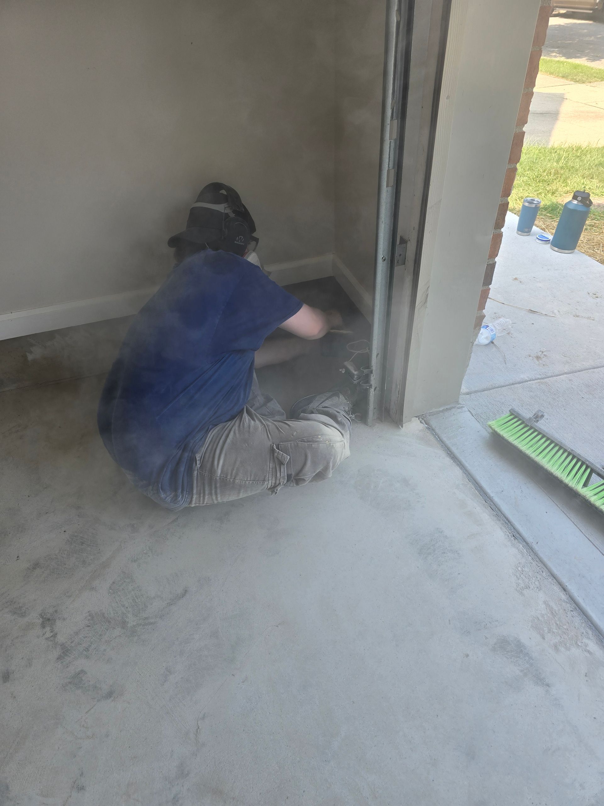 Worker kneeling in a room corner, smoothing concrete along the wall with a trowel during floor finishing.