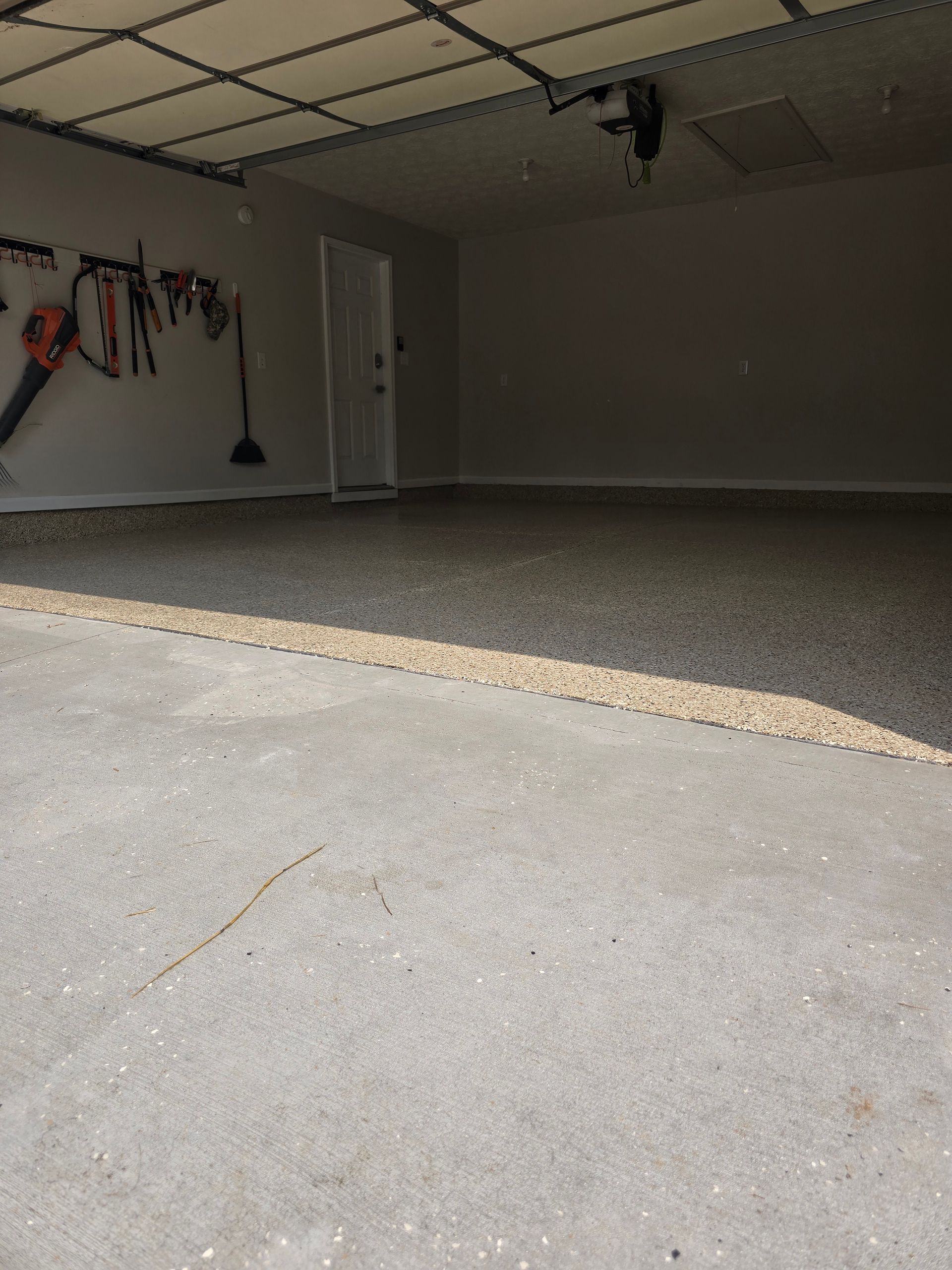 Empty residential garage with concrete floor, white walls, and tools hanging on the left wall.