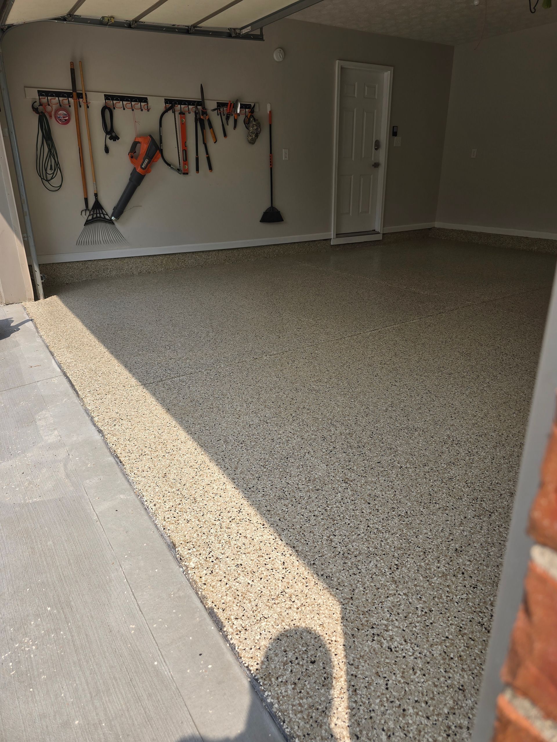 Carpeted garage interior with hanging tools on the back wall and a closed white door.