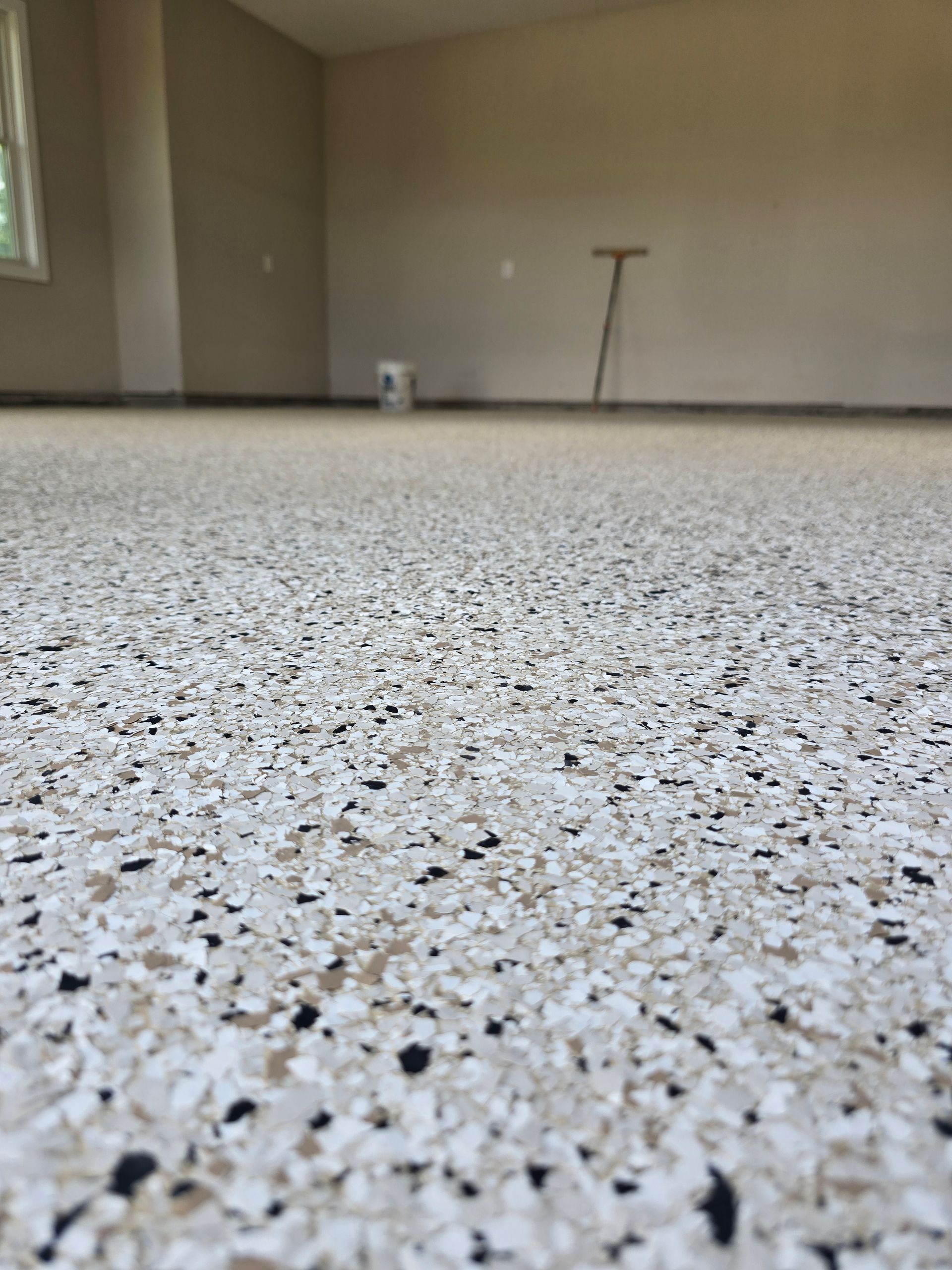 Speckled epoxy garage floor with beige walls and a small bucket in the background