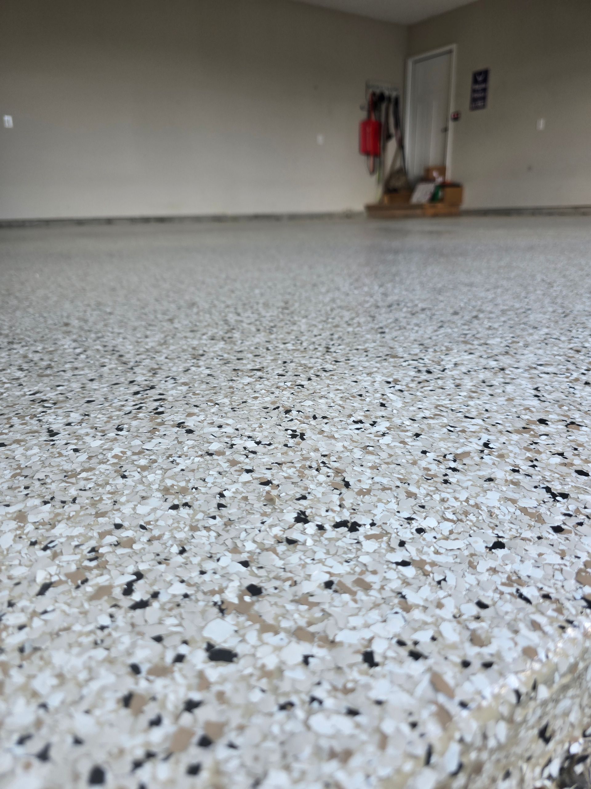 Speckled epoxy garage floor leading to a closed garage door with tools in the corner