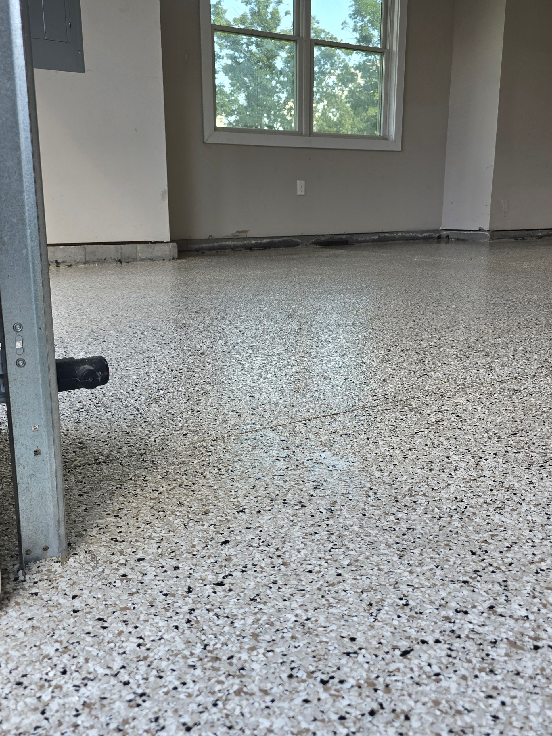 Empty room with speckled floor, gray walls, and a window letting in daylight.