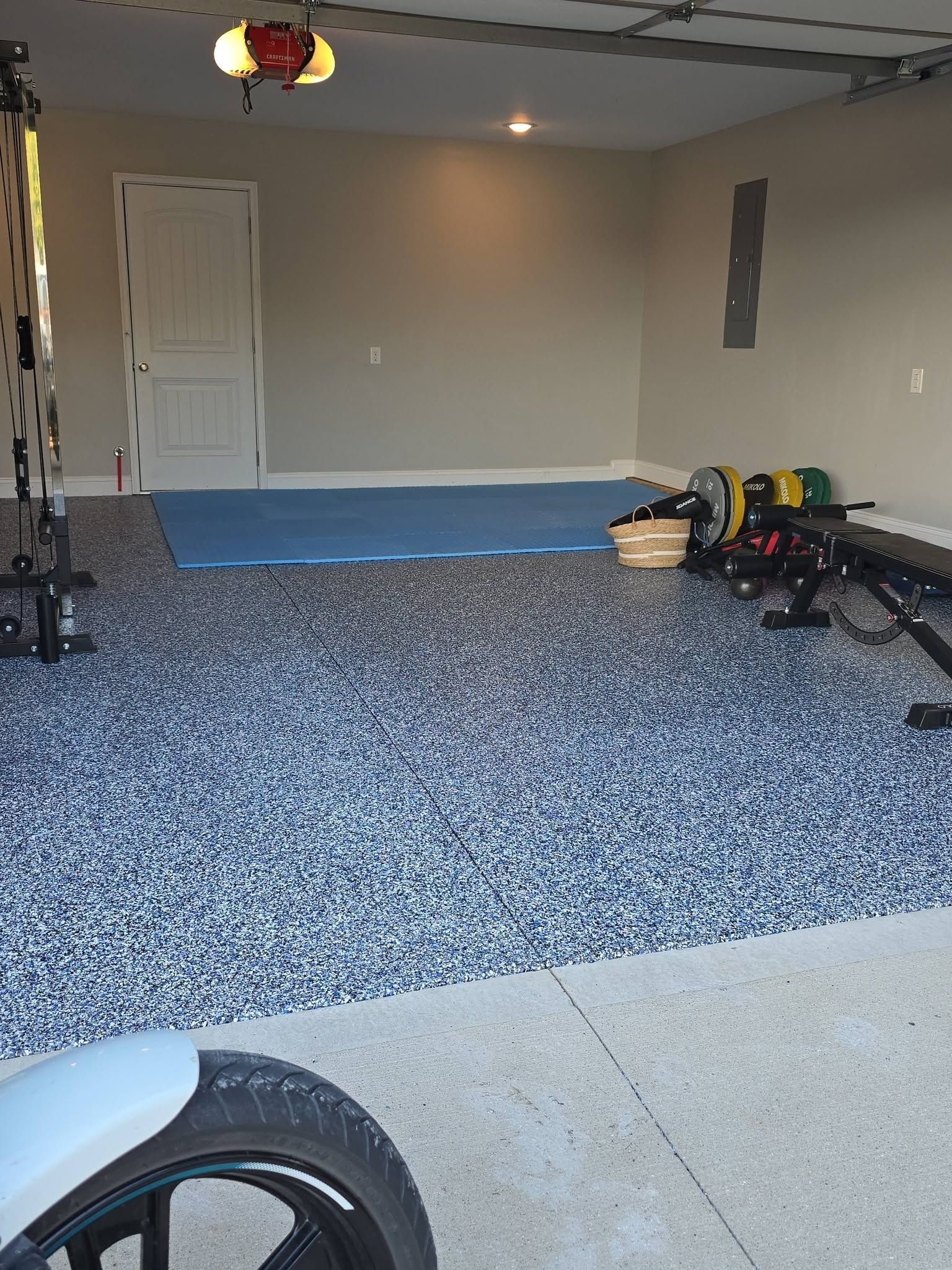 Empty garage with blue-speckled floor, open door, and gym equipment along the right wall