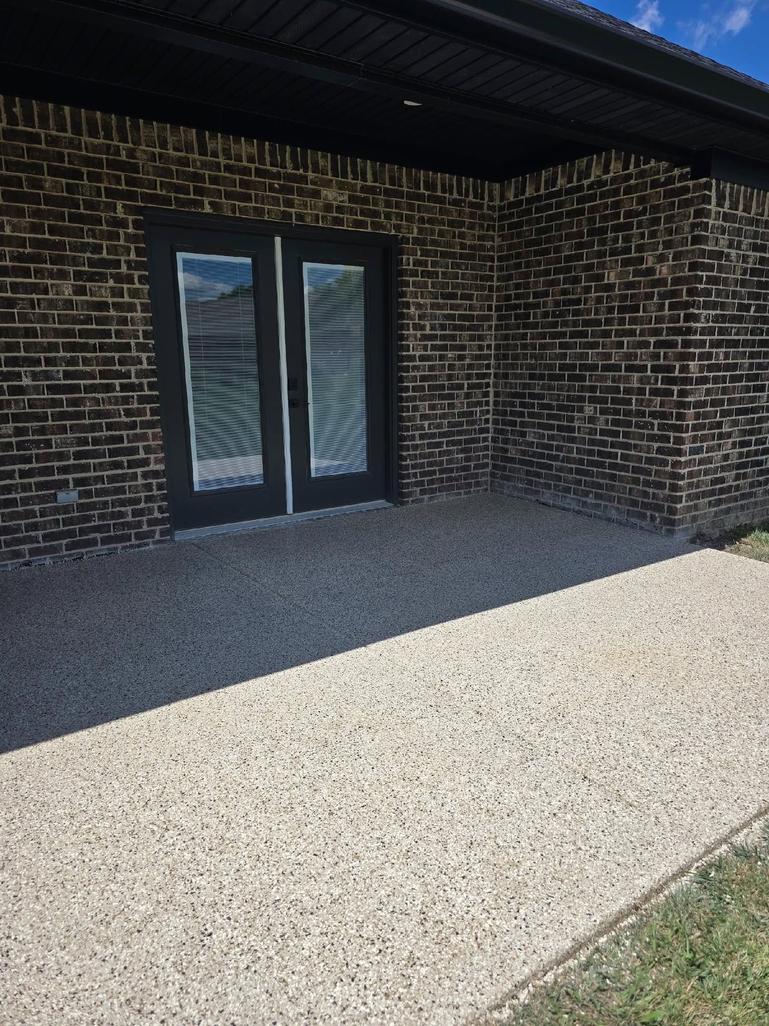 Brick house exterior with black-framed glass double doors and a gravel patio under a roof overhang