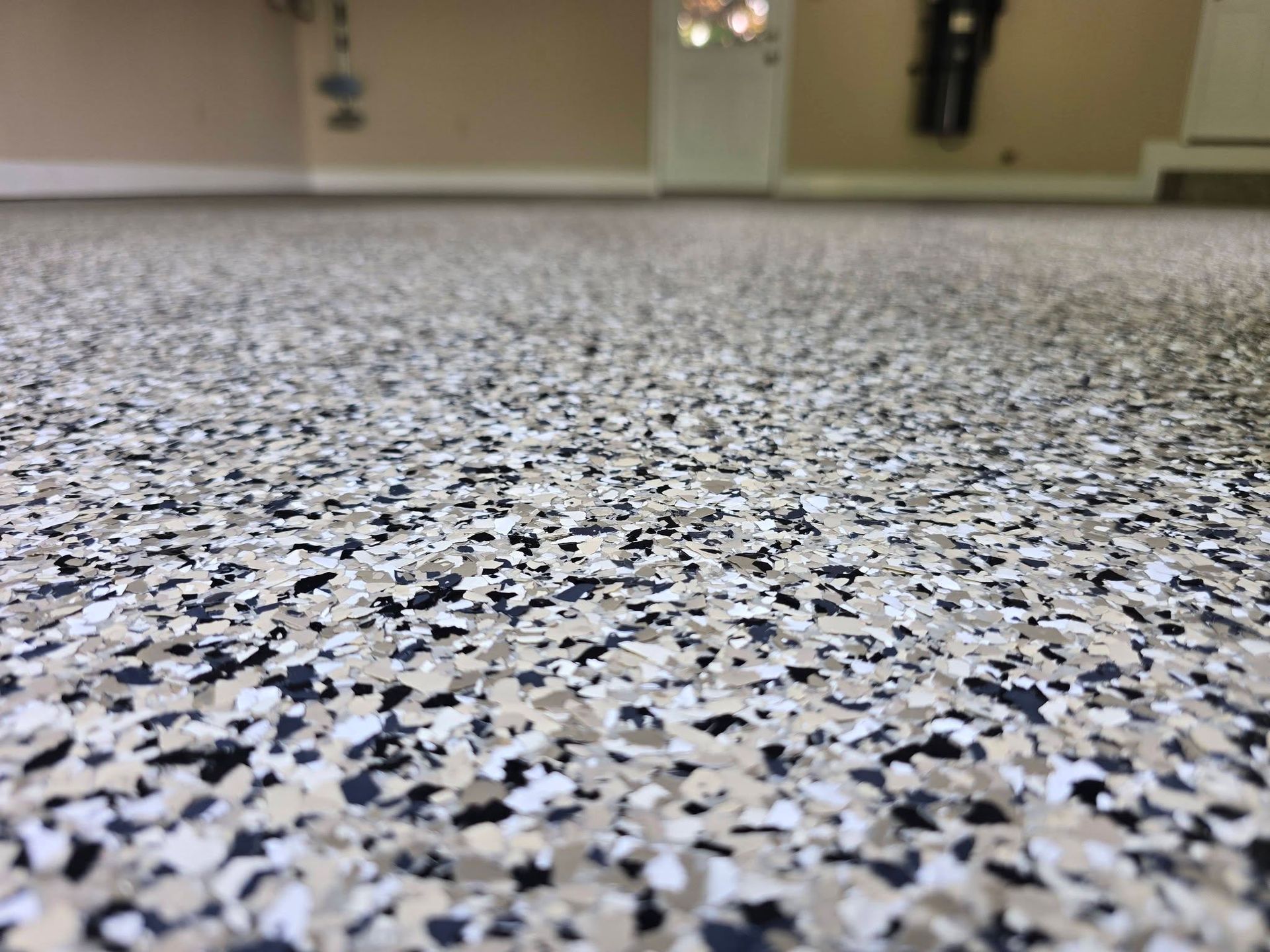 Close-up of a speckled gray epoxy floor in an indoor room, with a blurred hallway in the background