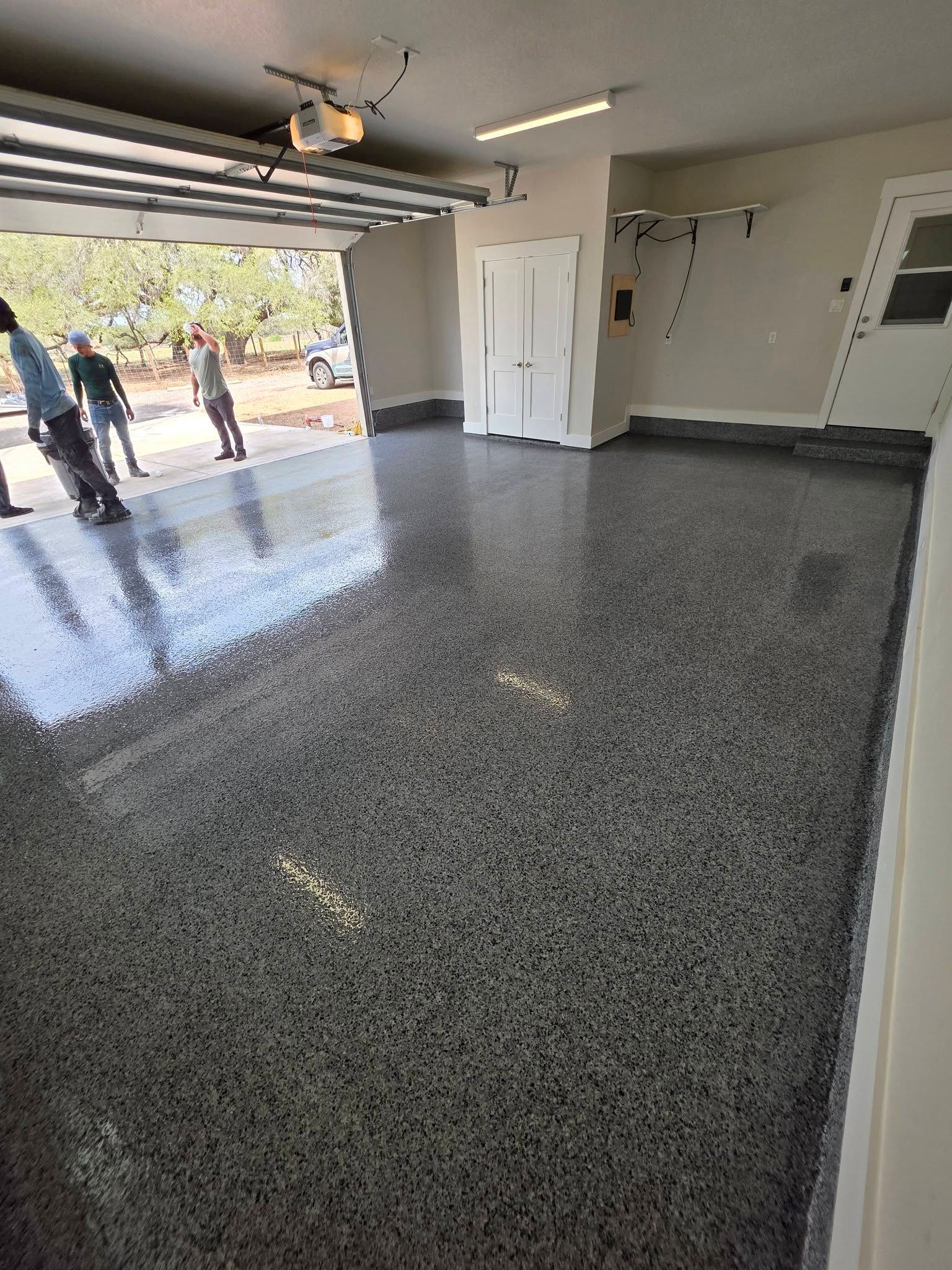 Empty garage with glossy speckled floor, open door, and two people standing outside.