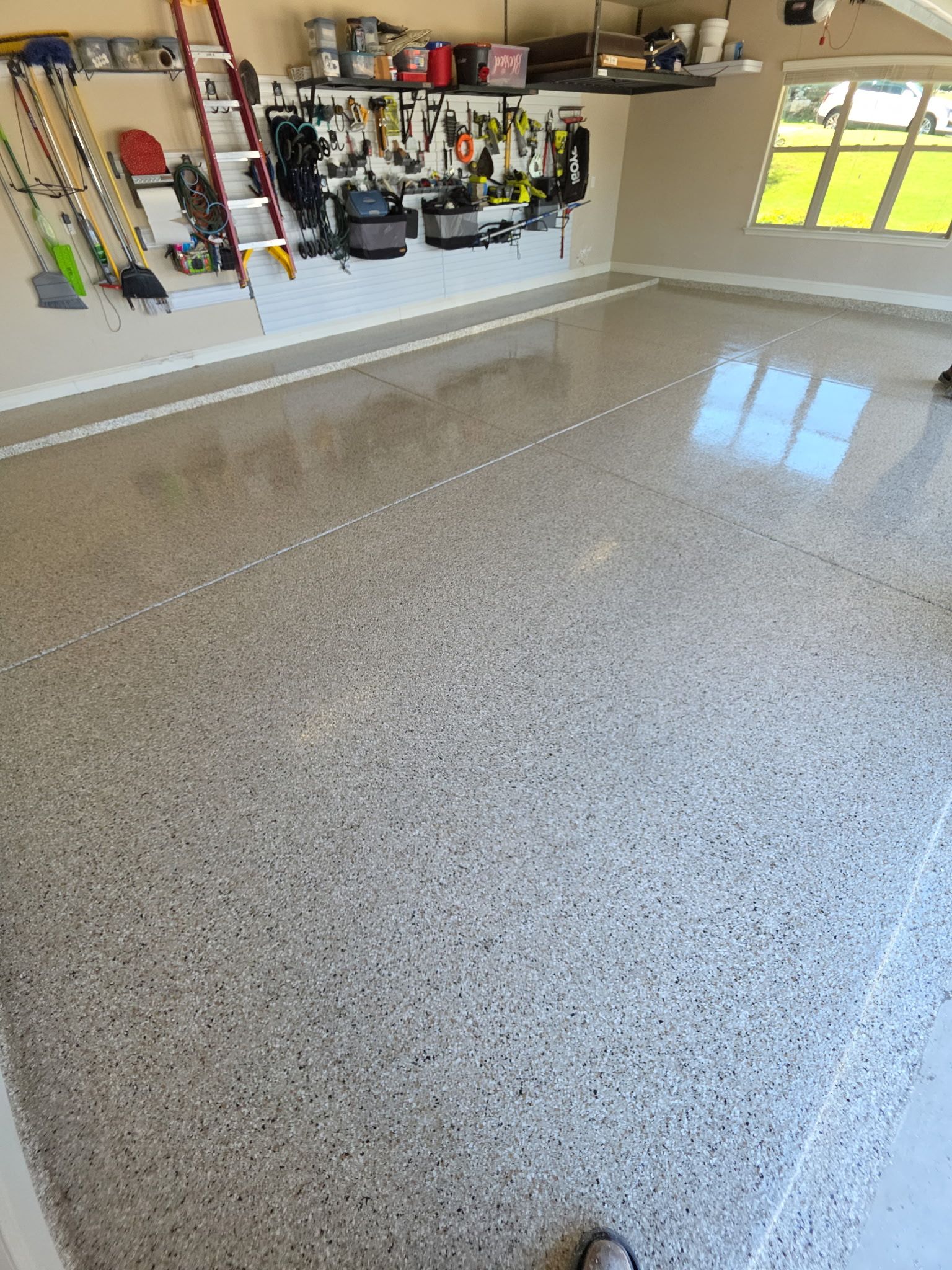 Garage with glossy speckled epoxy floor and wall-mounted tools and storage shelves.
