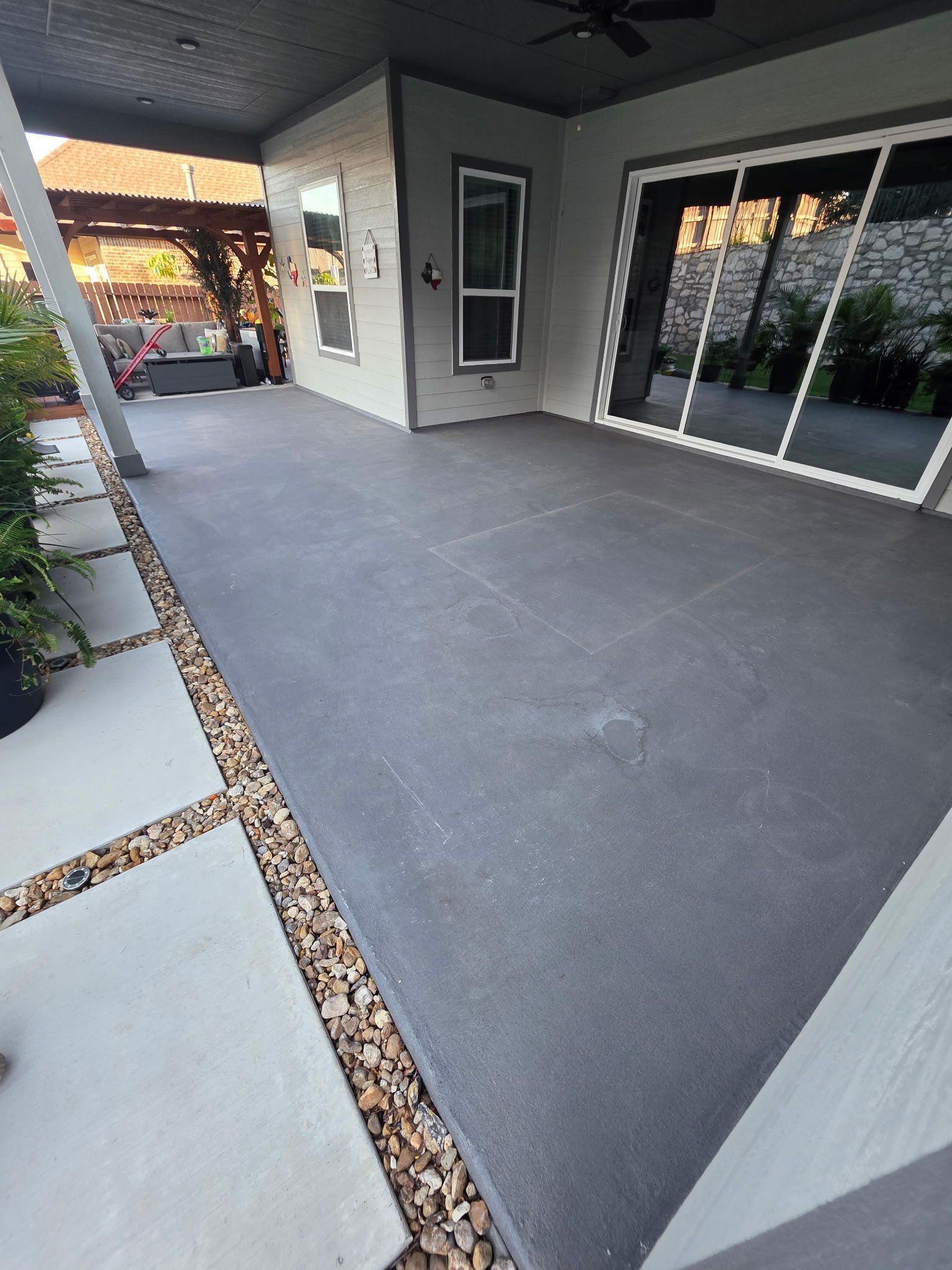 Modern covered patio with gray concrete floor, black-framed windows, and sliding glass doors.