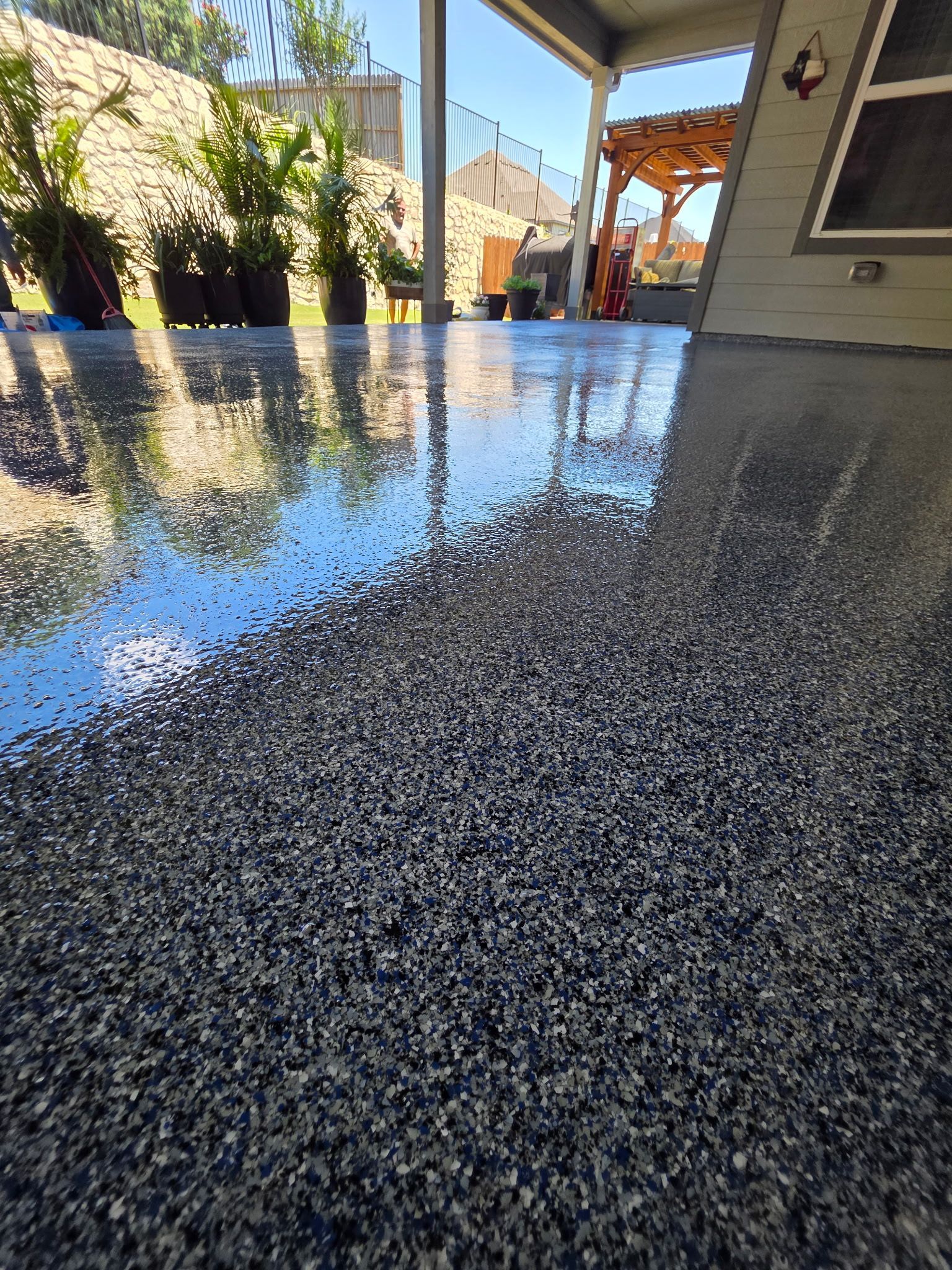 Close-up of a glossy black speckled tabletop reflecting a blue sky and patio setting