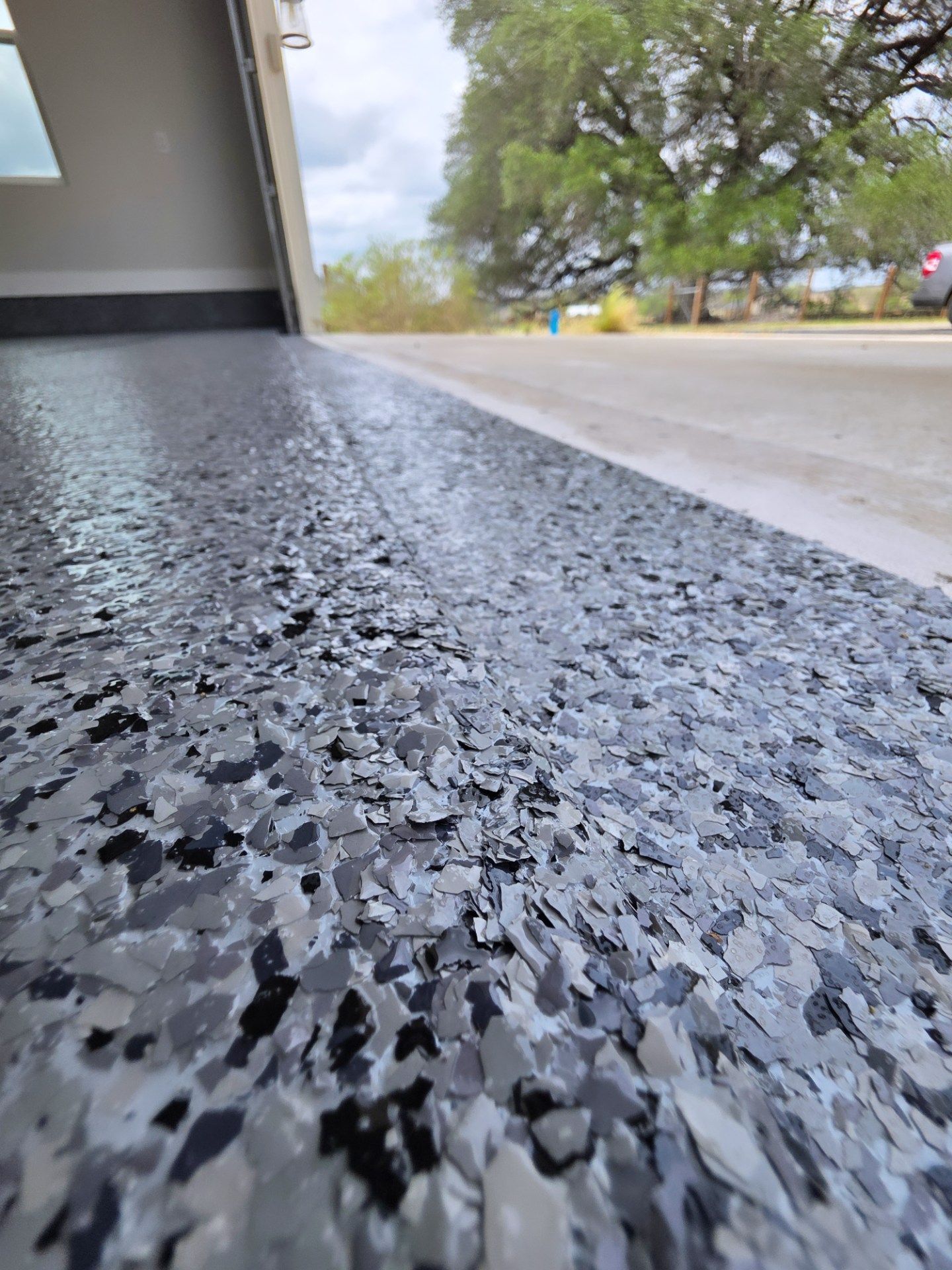 Low-angle view of a speckled concrete floor beside a driveway and trees outdoors