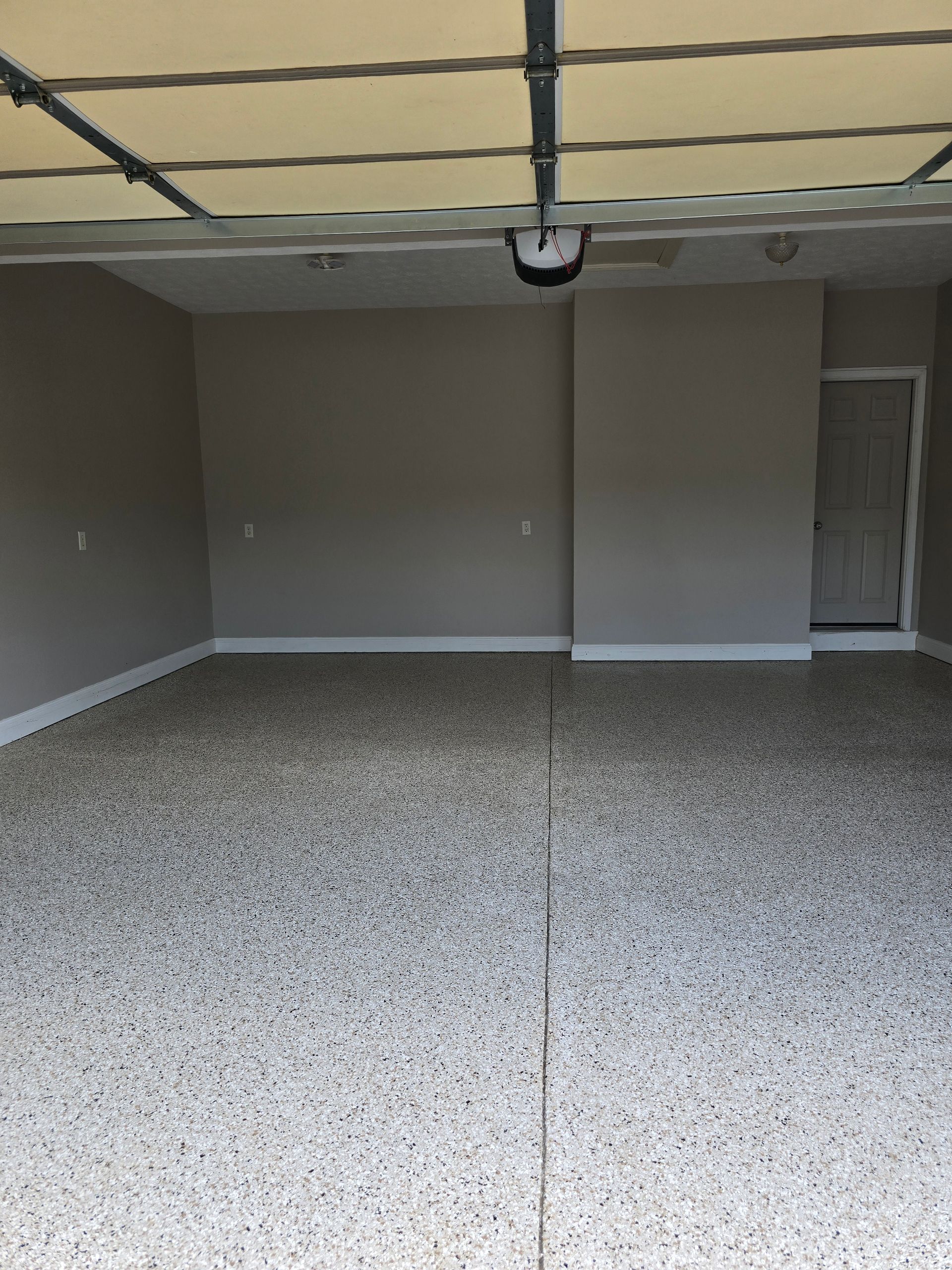 Empty garage with gray walls, speckled floor, and open overhead door view.