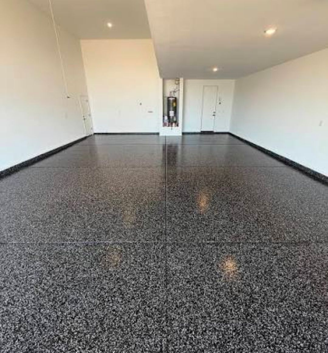 Empty garage with black speckled epoxy floor and white walls, viewed from one end.