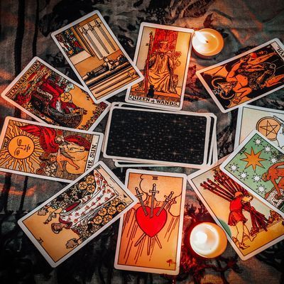 Cartes de tarot étalées, le jeu central face cachée. On y trouve la Reine de Bâtons et le Trois d'Épées. Des bougies allumées de chaque côté.