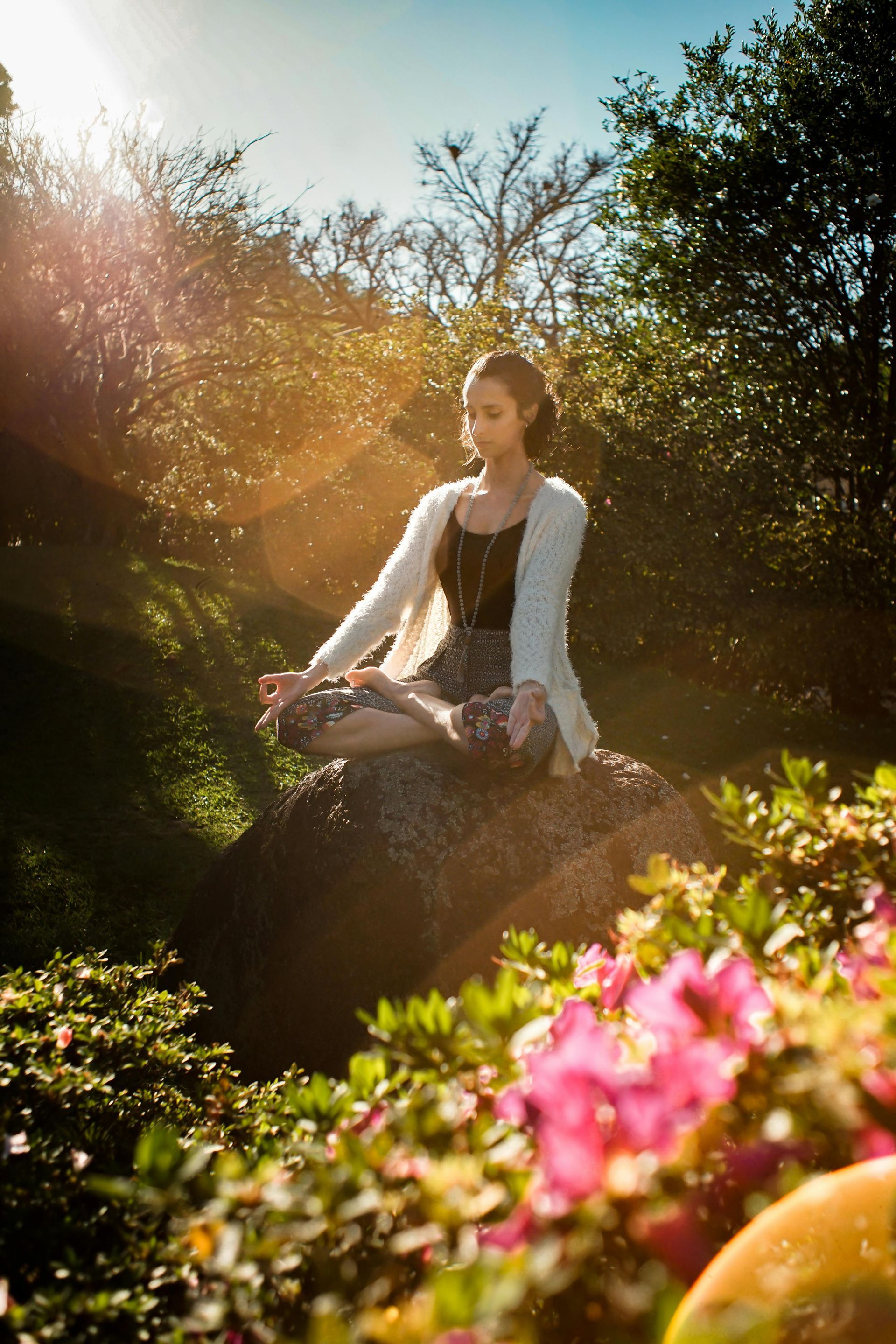 Femme méditant dans un jardin, jambes croisées, mains sur les genoux, sous la lumière du soleil.