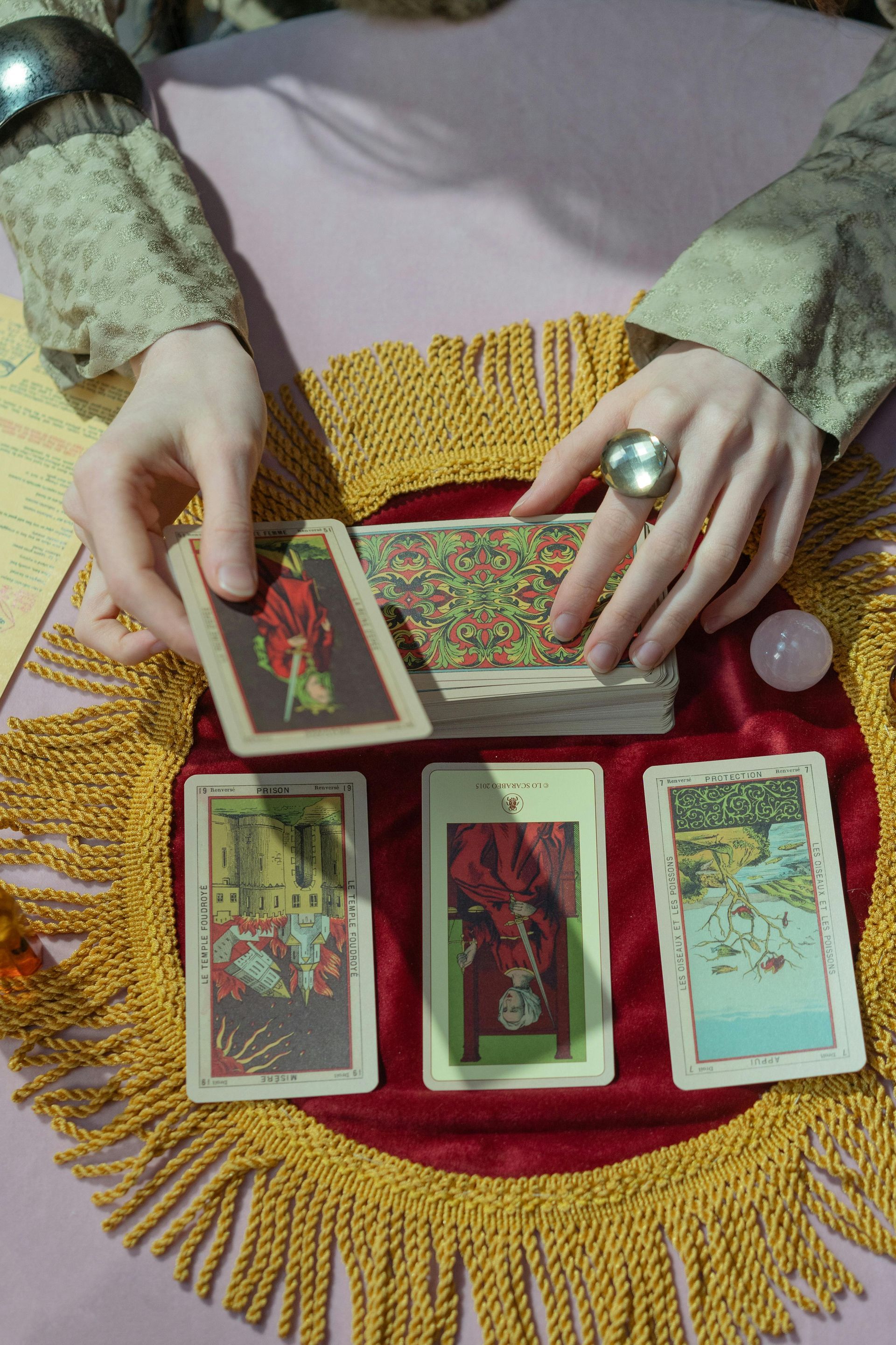 Une personne mélange des cartes de tarot sur une table où trois cartes sont disposées.