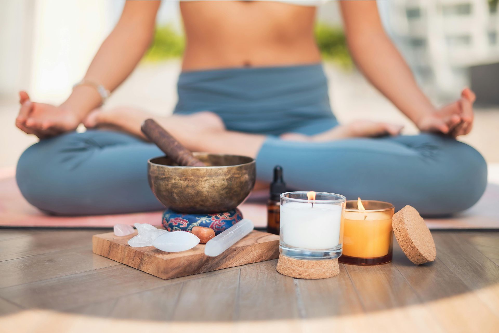Une personne médite sur un tapis de yoga, avec des bougies, un bol et des cristaux.