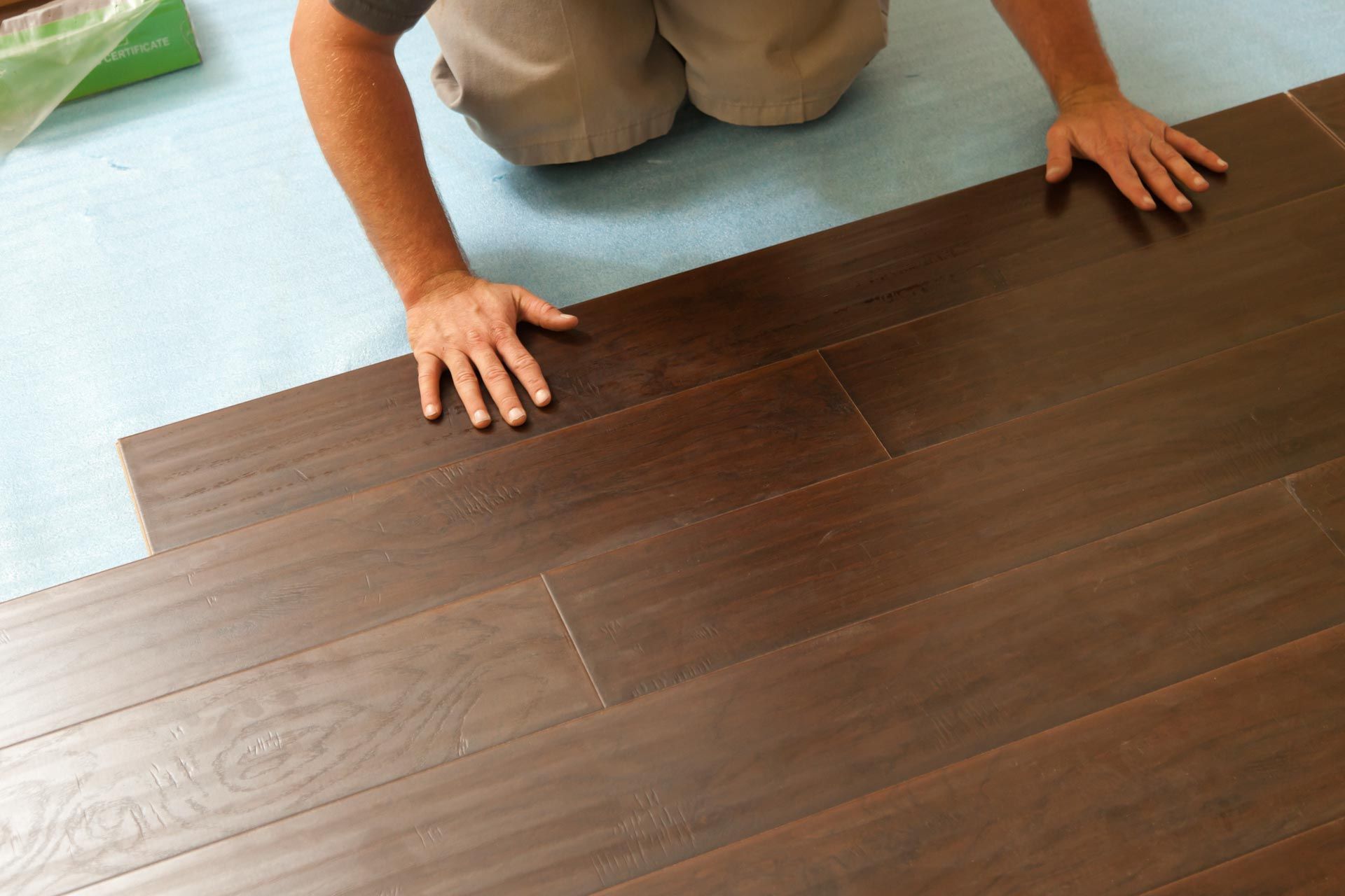 A person is laying a piece of wood on a hardwood floor.